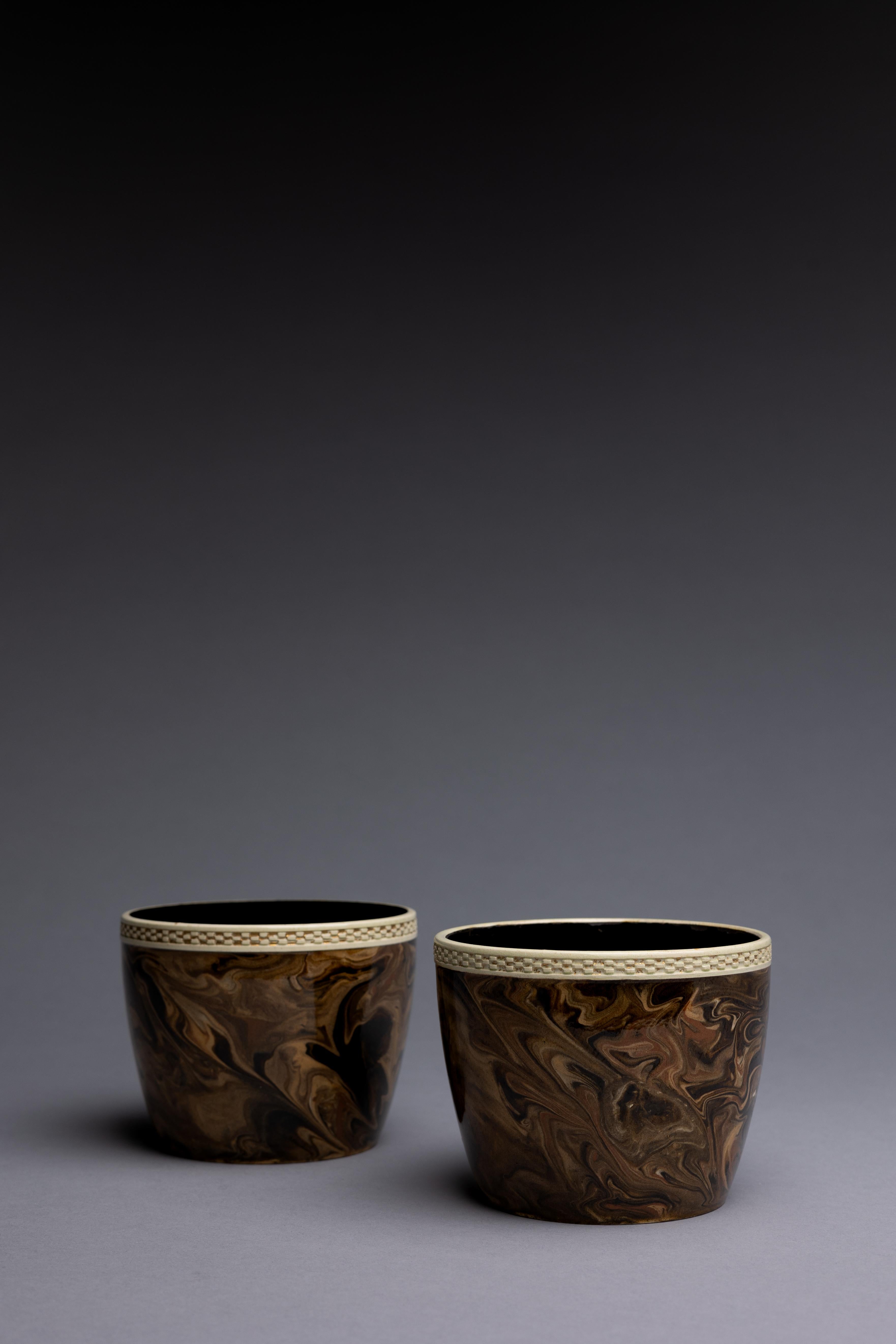 A pair of plant pots covered in marbled brown glaze emulating agate gemstone encircled with checkered rims accented in gold, made circa 1770 by Wedgwood & Bentley in Staffordshire, England.

Emulating the mesmerizing marbled surface of a precious