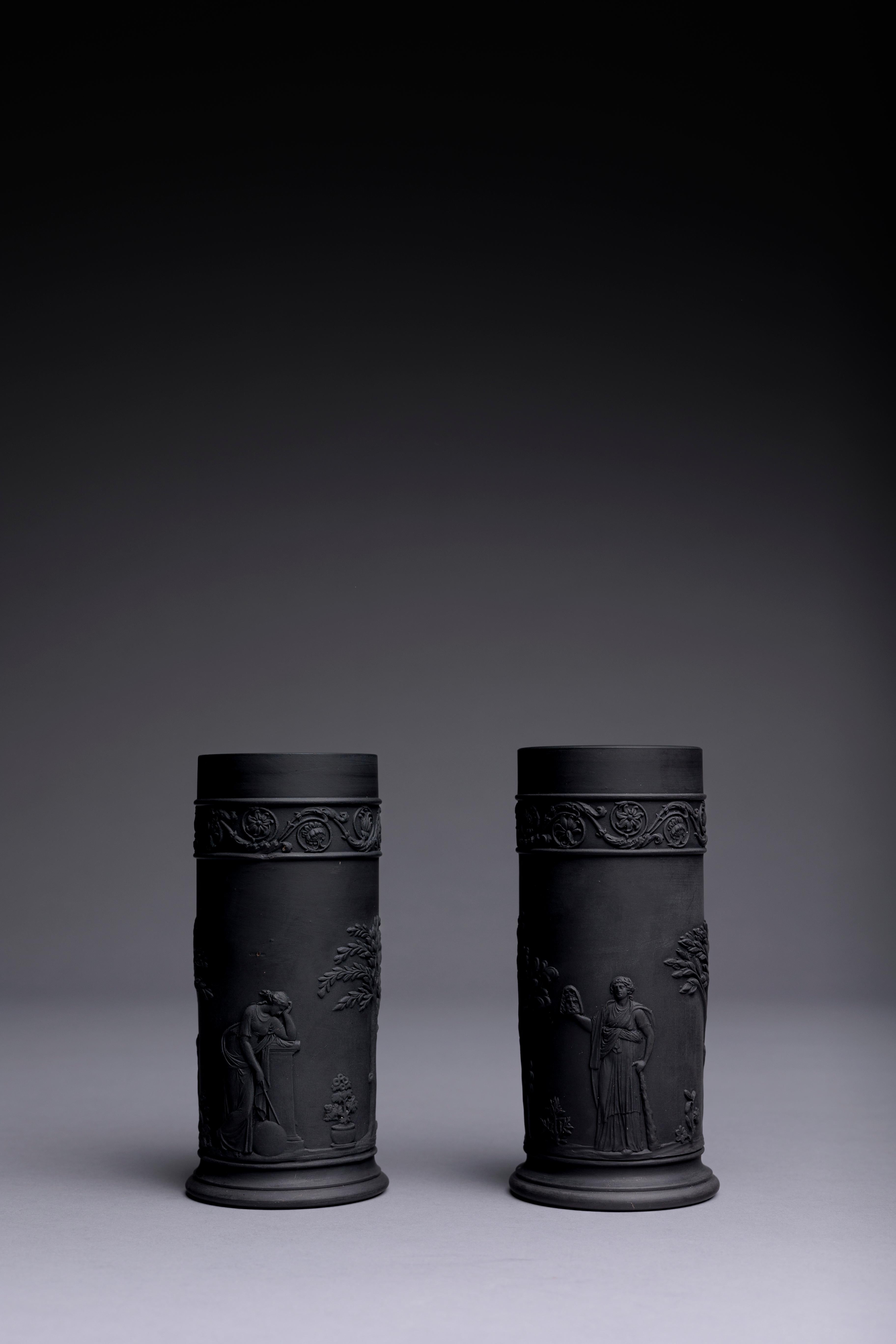 A pair of Neoclassical black basalt spill vases by Wedgwood, made circa 1820.

The vases are accented with a delicate border of scrolling acanthus leaves and depict excerpts from John Flaxman’s Apollo and the Muses. Apollo with his lyre; Thalia,