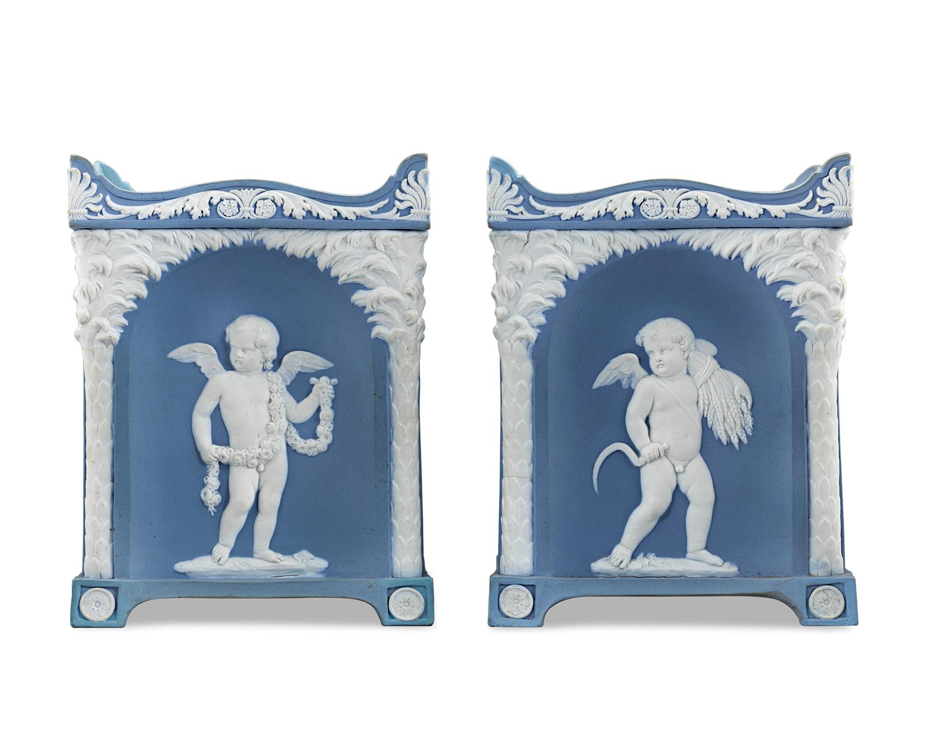 Crafted by Wedgwood, this exquisite and rare pair of square-section bulb pots are comprised of the firm’s famous pale “Wedgwood blue” jasperware so prized by collectors and connoisseurs alike. Winged, putti-like cupid figures adorn each pot’s four