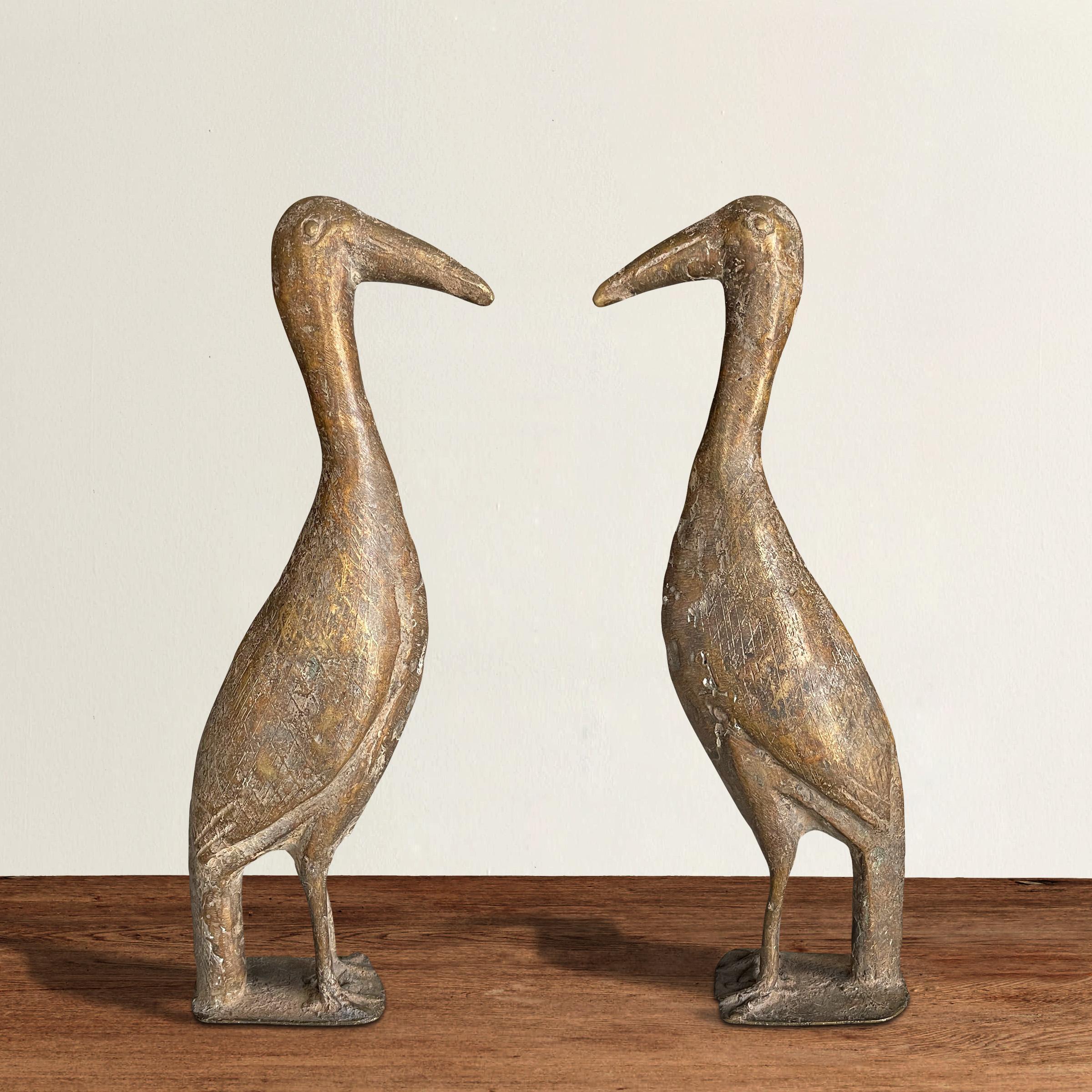 An arresting pair of 20th century West African cast bronze bird sculptures, each with incised feathers, raised eyes, and standing on two legs, resting on flat bases. Perfect for decorating your mantel or bookshelves!
