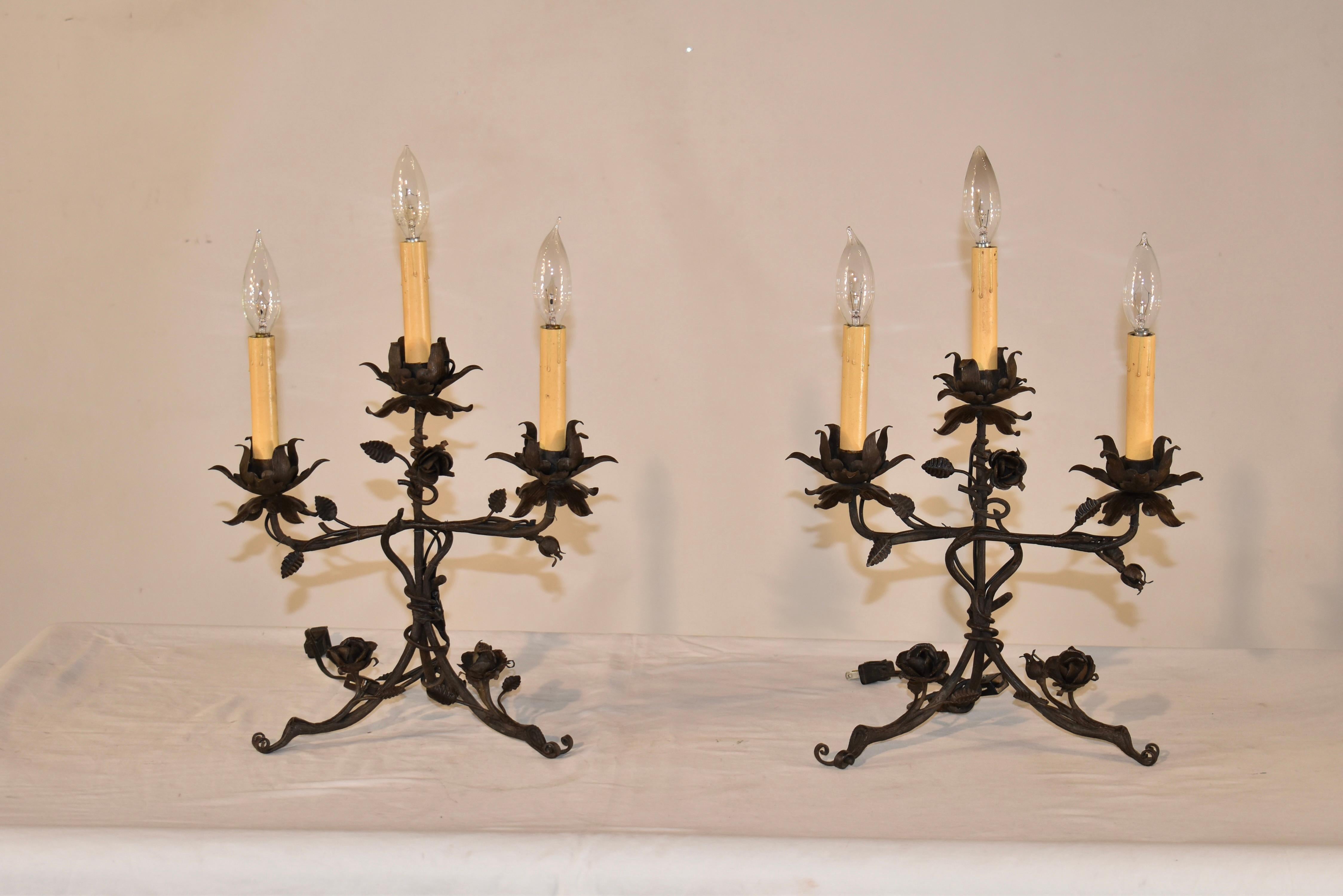 Insolita coppia di candelabri a tre luci in ferro battuto, a forma di vite con fiori e boccioli lavorati a mano.  Le tre luci sono alloggiate in coppe per candele floreali per un look affascinante su qualsiasi tavolo o caminetto.  I candelabri sono