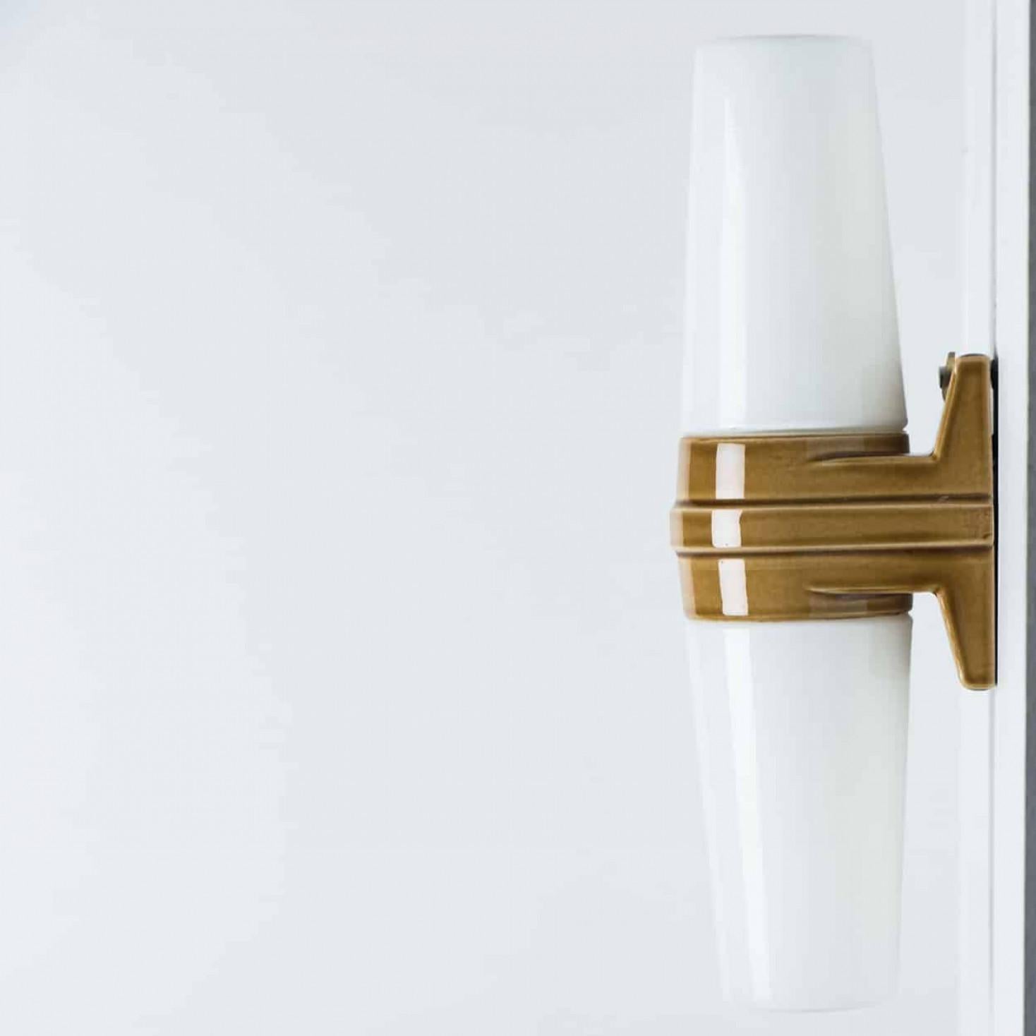 Splendide lampade da parete, realizzate in Svezia intorno agli anni '70. Le luci sono composte da due coppe di vetro bianche a forma di cono, tenute insieme da una fascia di ceramica marrone al centro, creando un effetto di classe ed