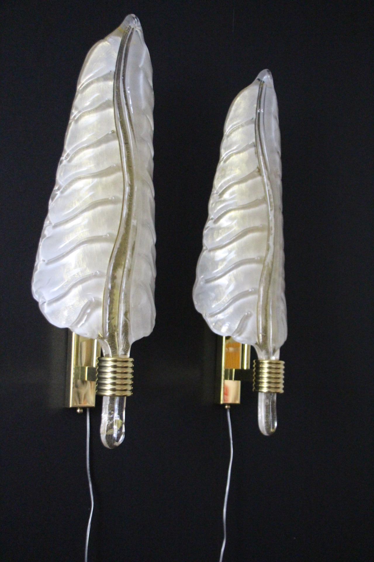 This is a very nice pair of pearly milk white blown Murano glass sconces in a shape of a leaf or a feather on a polished golden brass structure. Its curvy shape is very pleasant and realistic as we can see the detailed leaf veins. Their main vein is