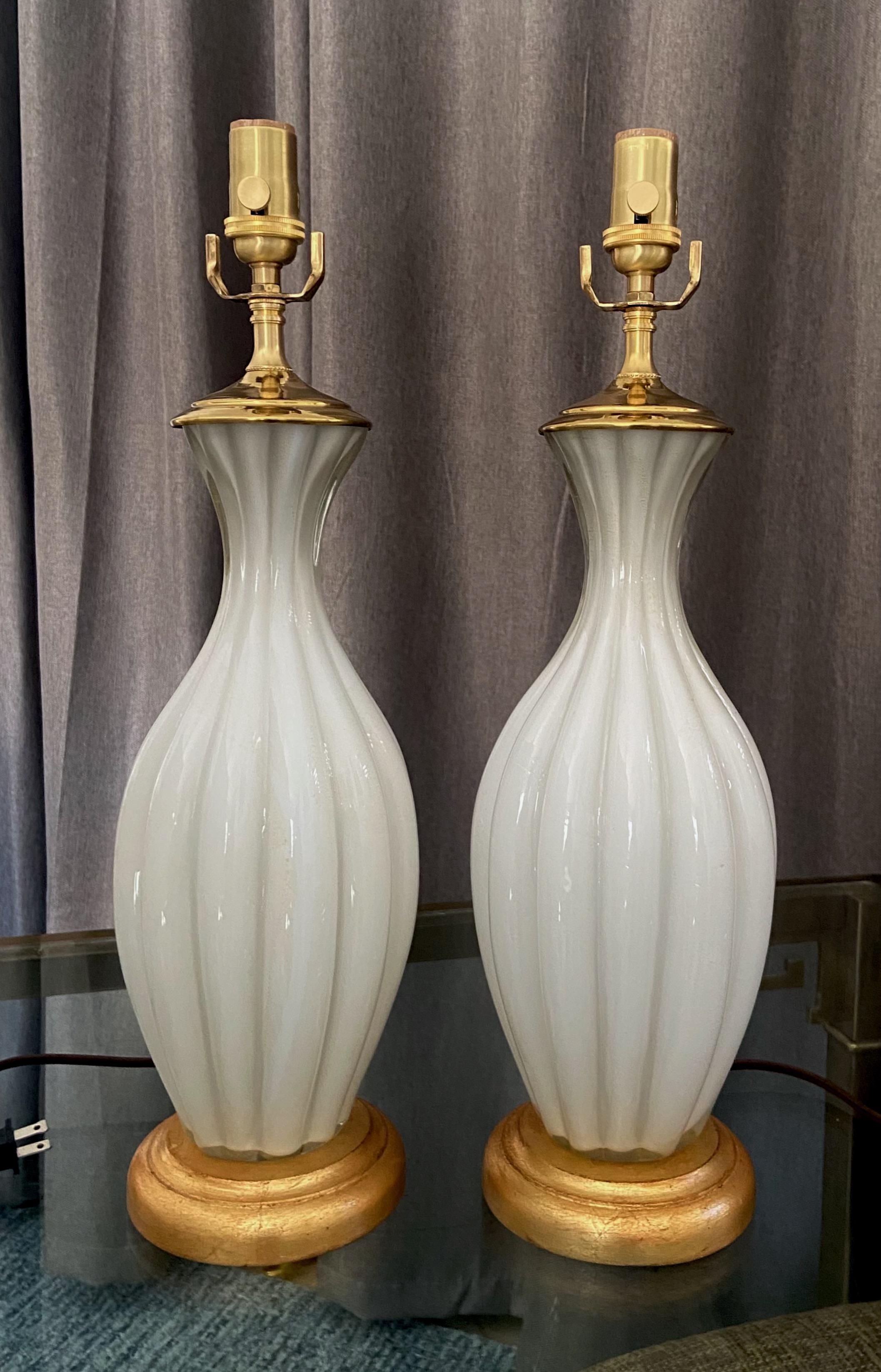 Pair of Murano Italian white cased glass ribbed lamps, mounted giltwood bases. The hand blown case has subtle flakes of gold inclusions. Newly wired for US with new
3-way sockets and rayon covered cords.

Measures: 14