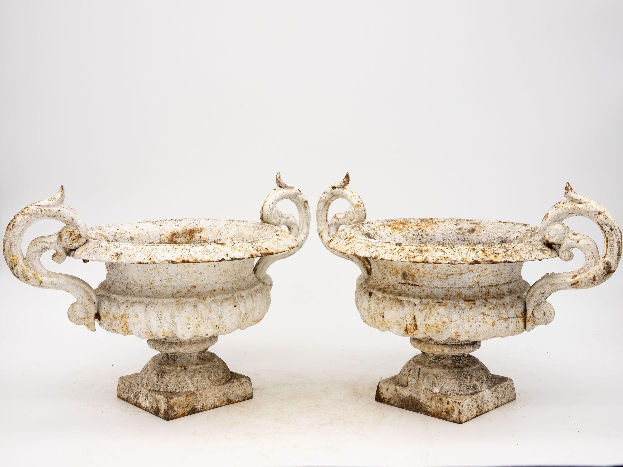 Exuding timeless elegance, this exquisite pair of late 19th-century French garden urns captures the essence of French garden design. Standing as guardians of history, each urn is adorned with timeworn white paint that has gracefully weathered over