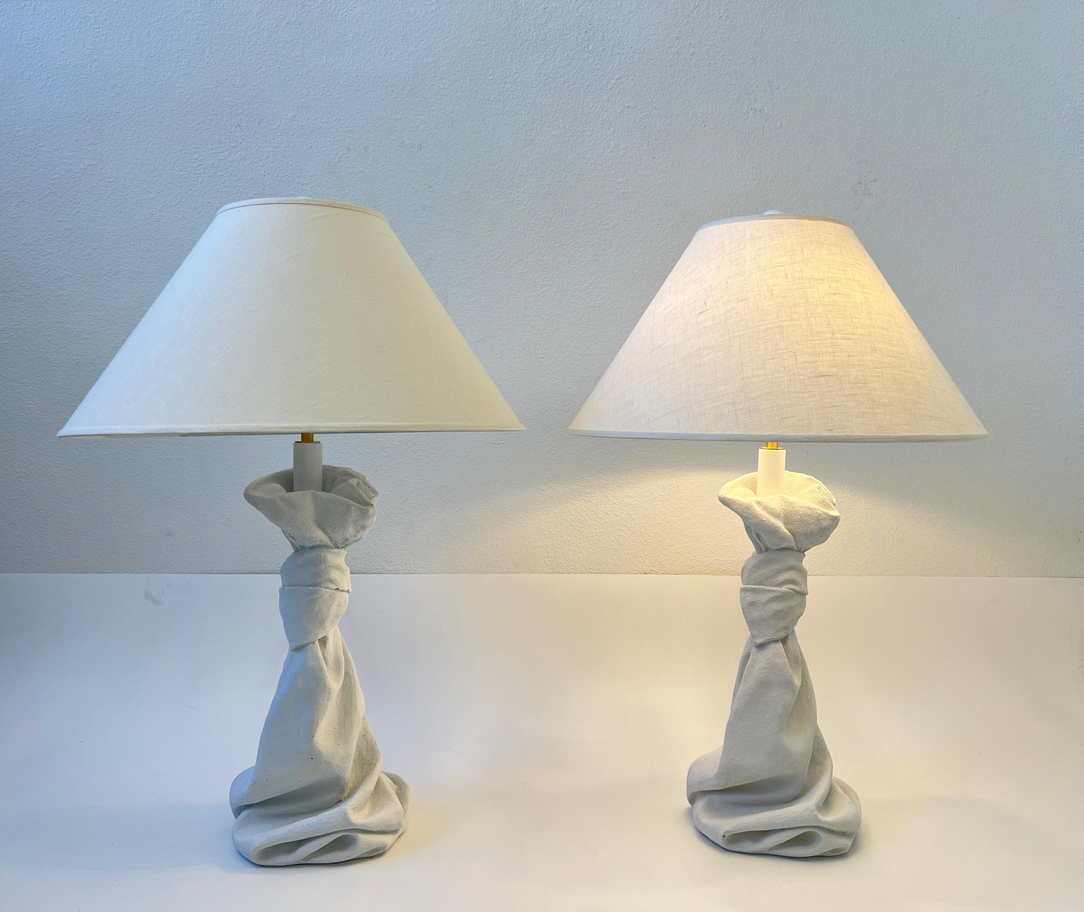 Glamorous pair of white draped plaster and satin brass table lamps in the style of John Dickinson. 
Newly rewired and new vanilla linen shades. 
They take two 75w max Edison lightbulb. 

Measurements: 22” Diameter 32.5” High.
Base is 10” Wide,