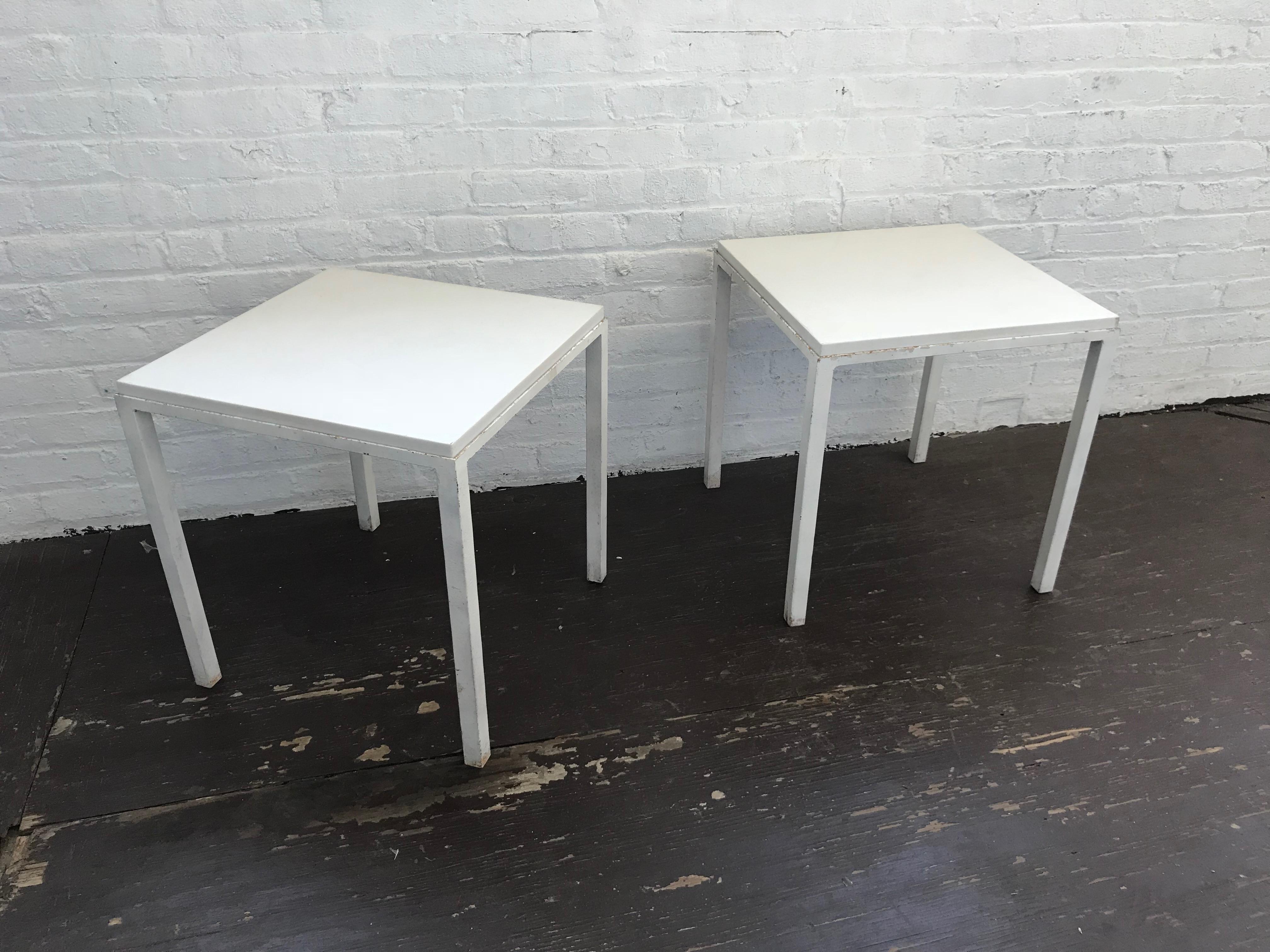 Pair of midcentury indoor / outdoor strong side or end tables in white powder coated metal each with slightly curved angles on the bottom edges where the legs meet the apron of the frame base and each with an inset, 1.125 inch thick polished white