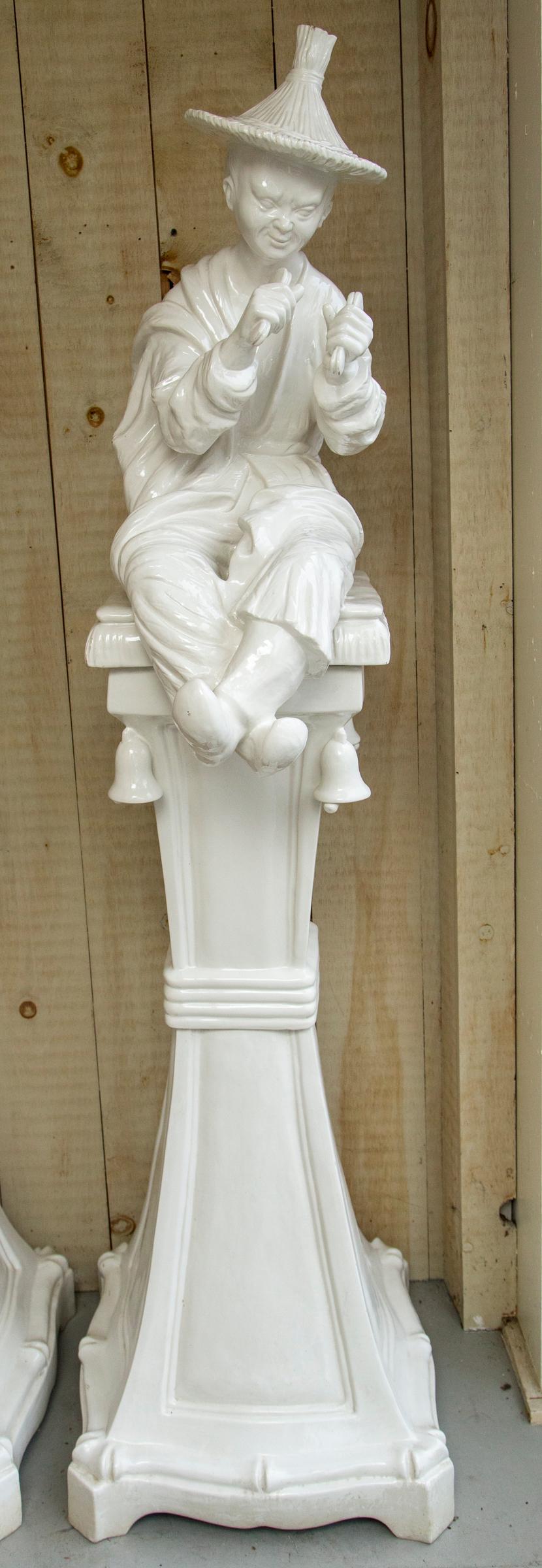 The white glaze over terracotta. Made in three sections, bottom of pedestal, middle of pedestal, and the figure atop. Concave sides, shaped square base. Bells hang from below the fronts of the figures. Paper tag says Italy.
The  figure wears a straw