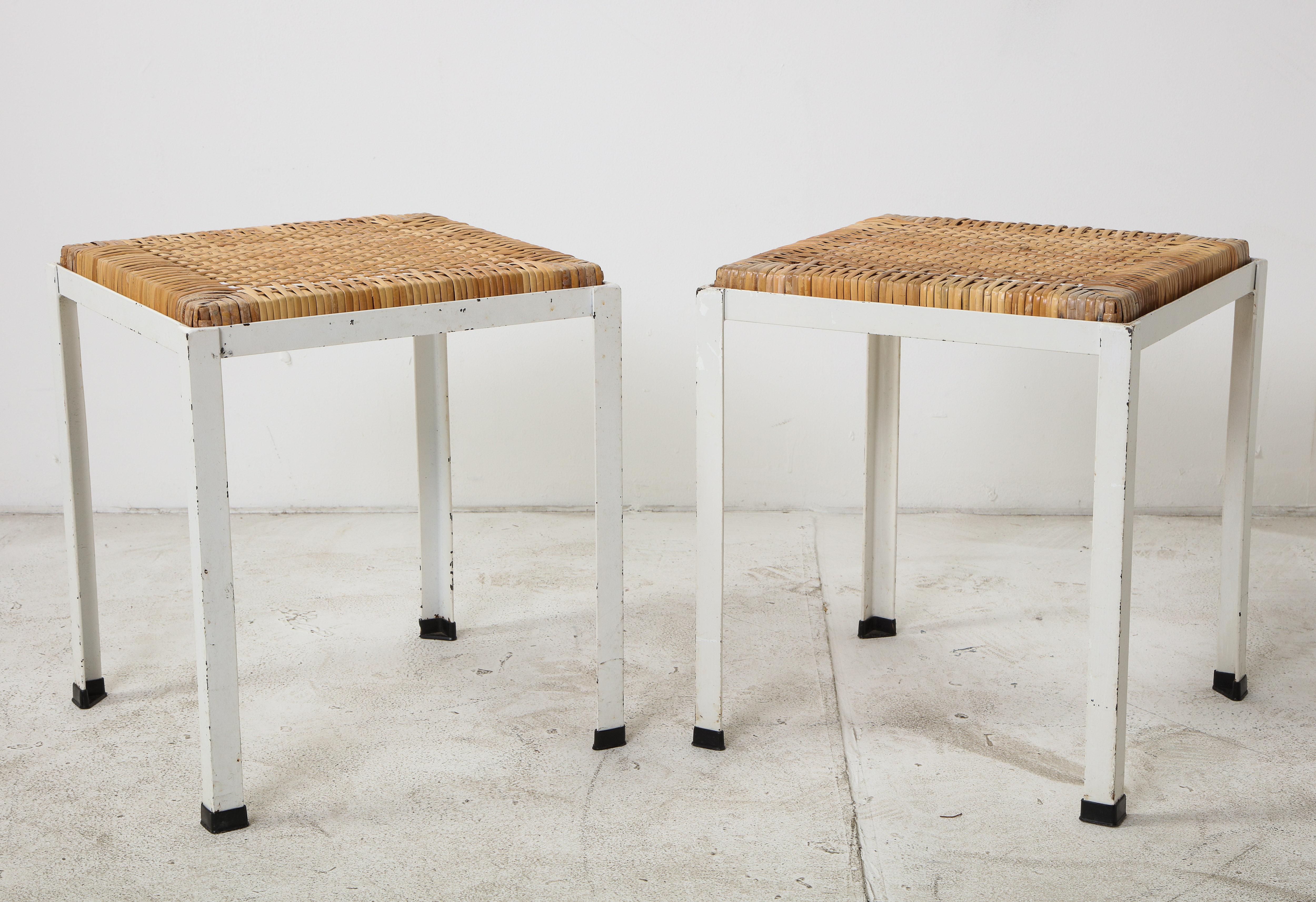 Pair of white painted iron stools with original rattan tops by Danny Ho Fong. Great for indoor/outdoor use. Plastic caps on feet so they will not scratch floors.