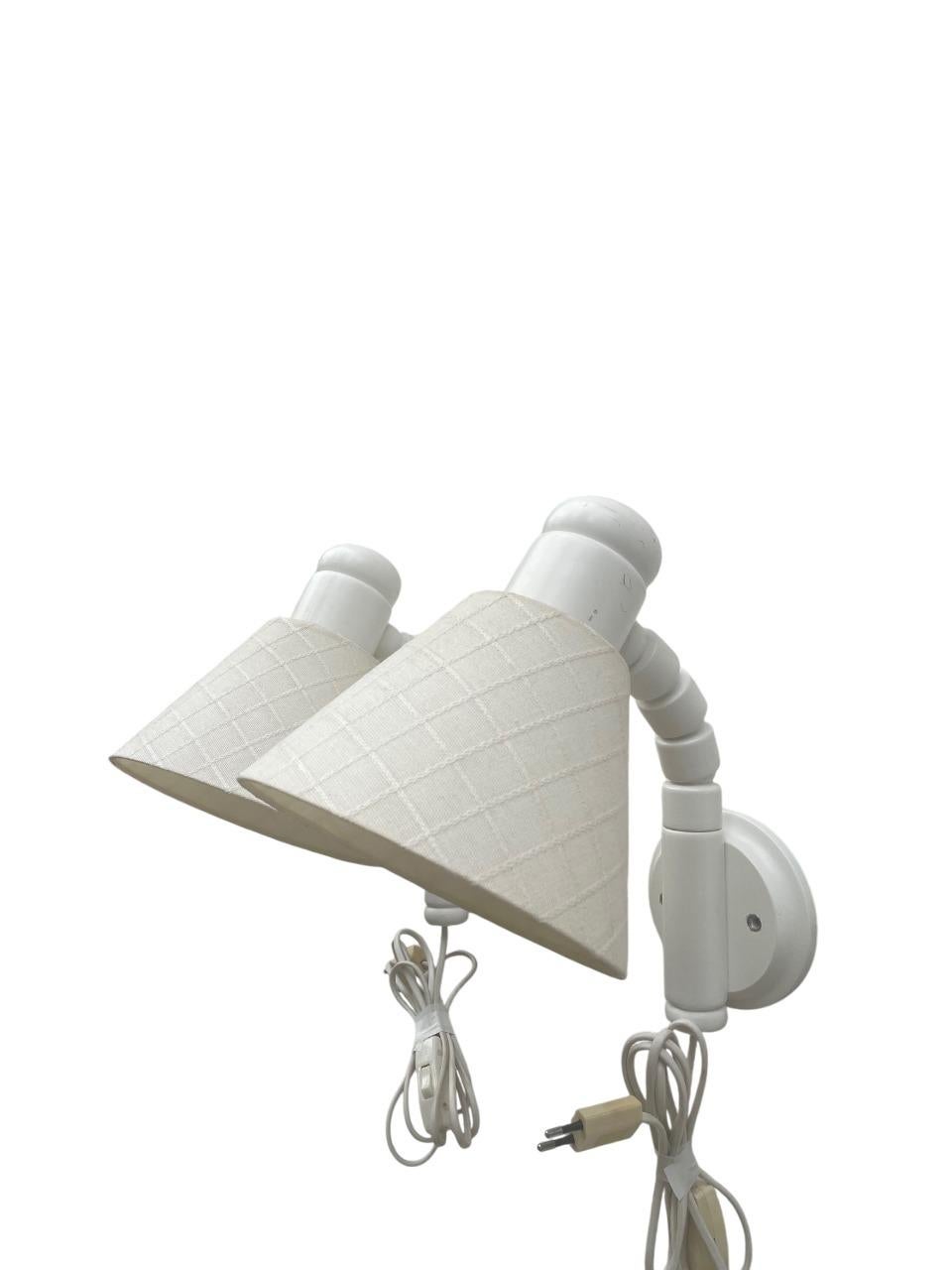 Beautiful pair of Swedish wall lamps by Solbacken Svarveri, crafted in solid pine and finished in white lacquered paint. The lamps feature flexible, ribbed pine arms and conical off-white fabric shades with a subtle checkered texture, characteristic