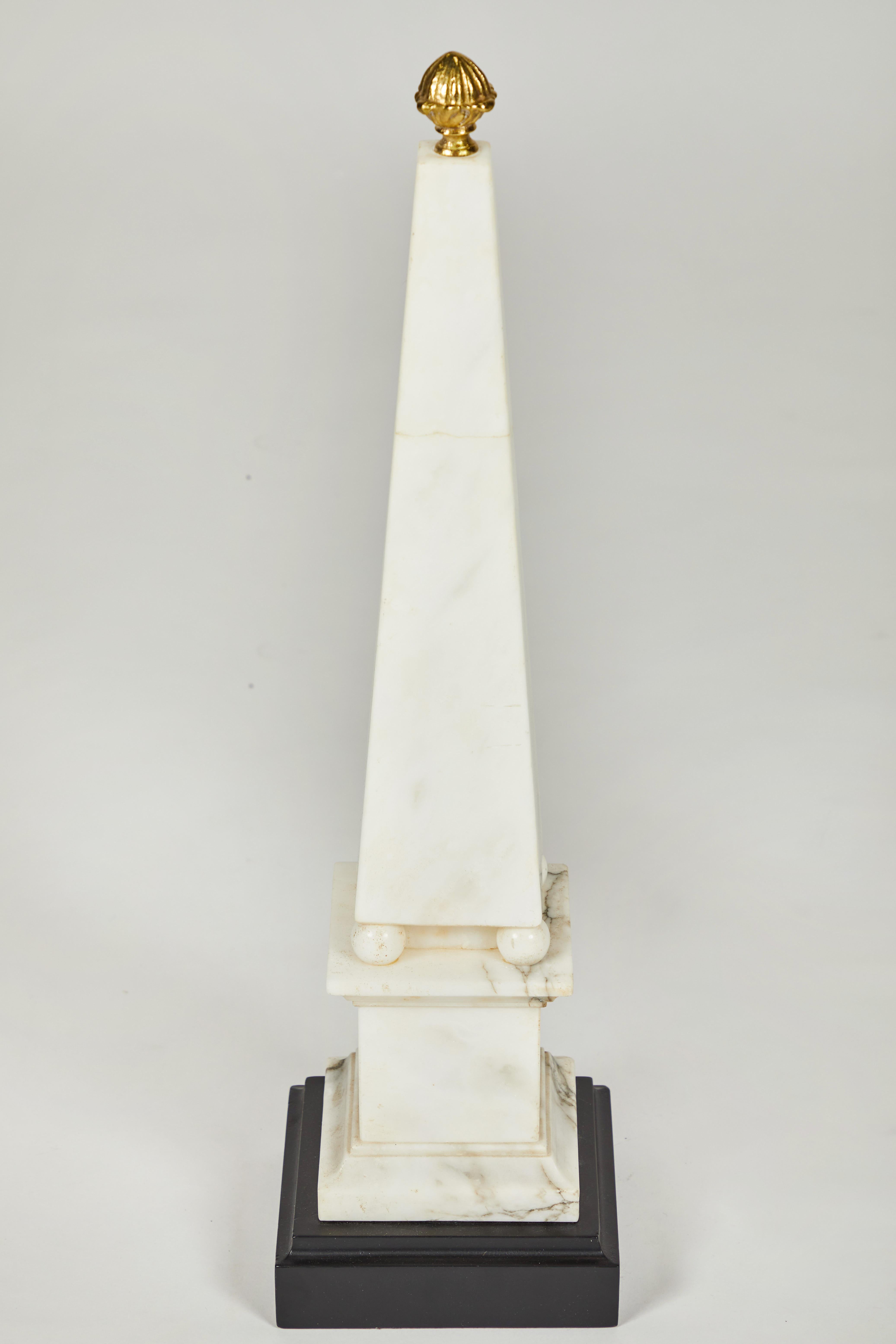 Pair of white marble obelisks on painted wood bases with brass acorn finials.