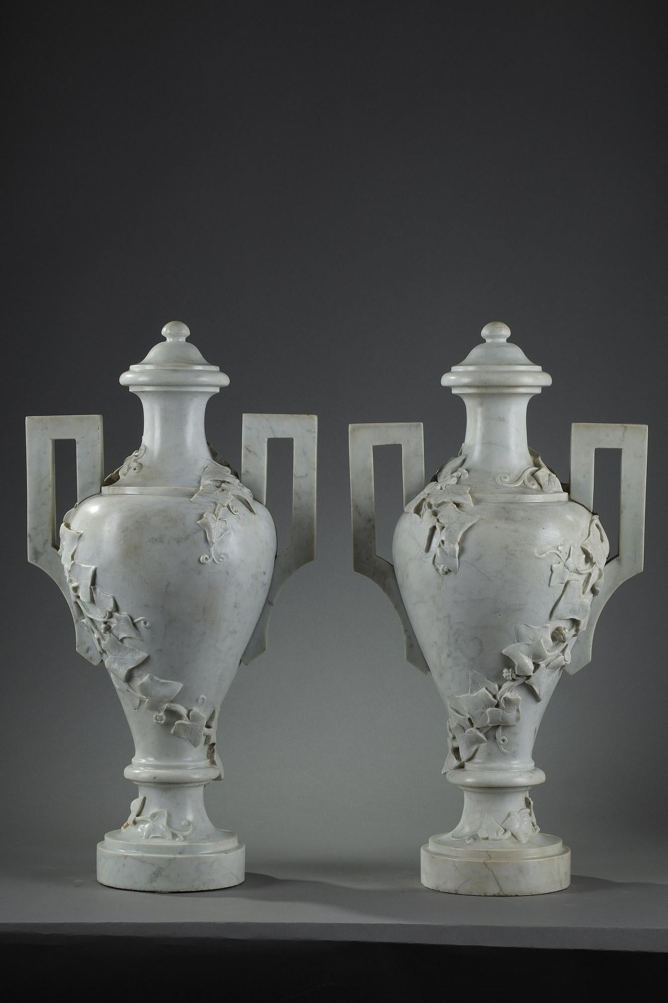 Große, abgedeckte Vasen mit Fuß aus weißem Carrara-Marmor in Form einer griechischen Amphore, geschnitzt mit kletterndem Efeu. Die Form der Griffe hat eine geometrische Form und zeigt den Geschmack des antiken Griechenlands im 18. Jahrhundert.