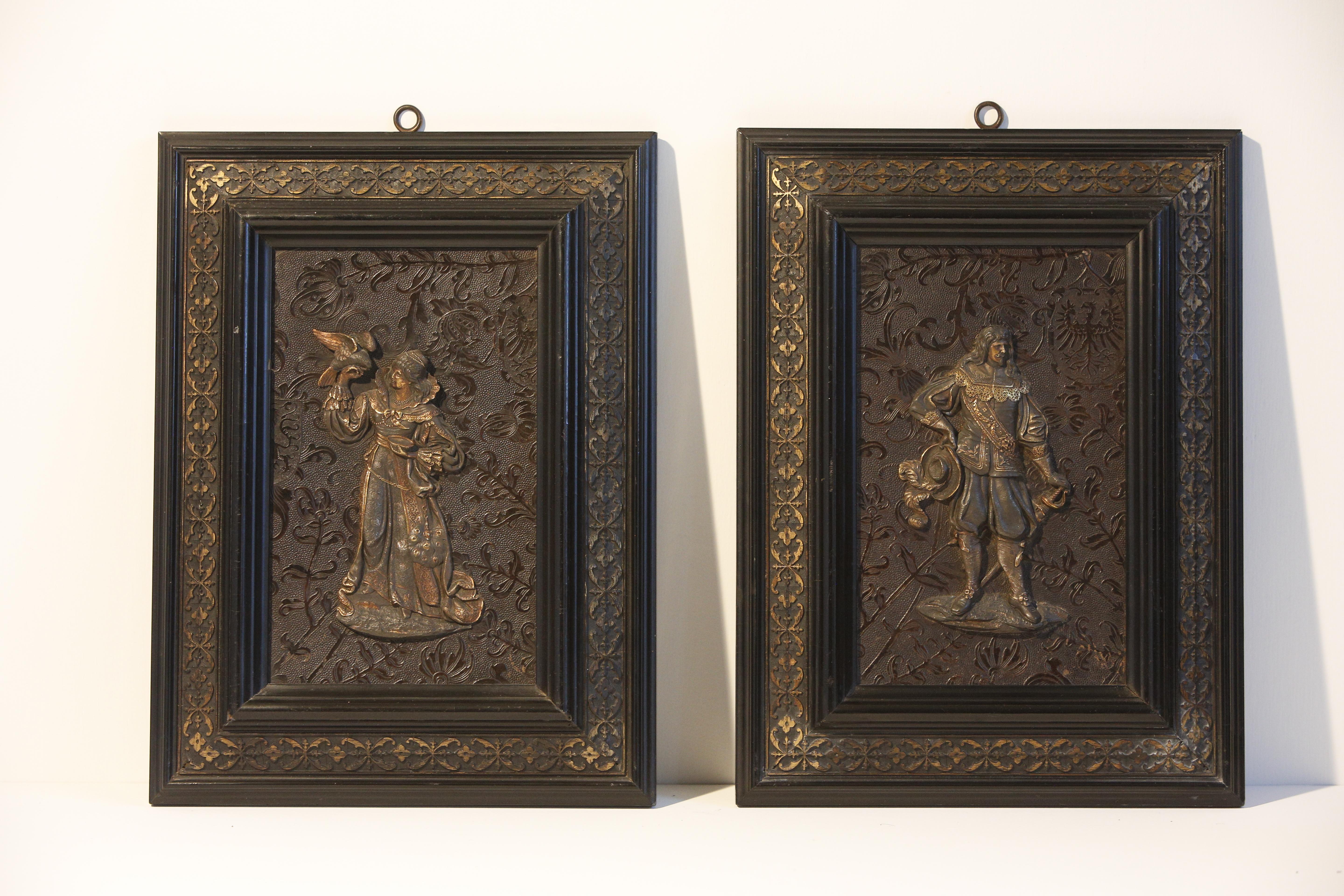 A pair of white metal and gilded bronze relief male and female figures in 17c costumes applied to an embossed decorative panel in ebonized frames. Little nicks and rubbings on the frames commensurate with age and use but otherwise in excellent