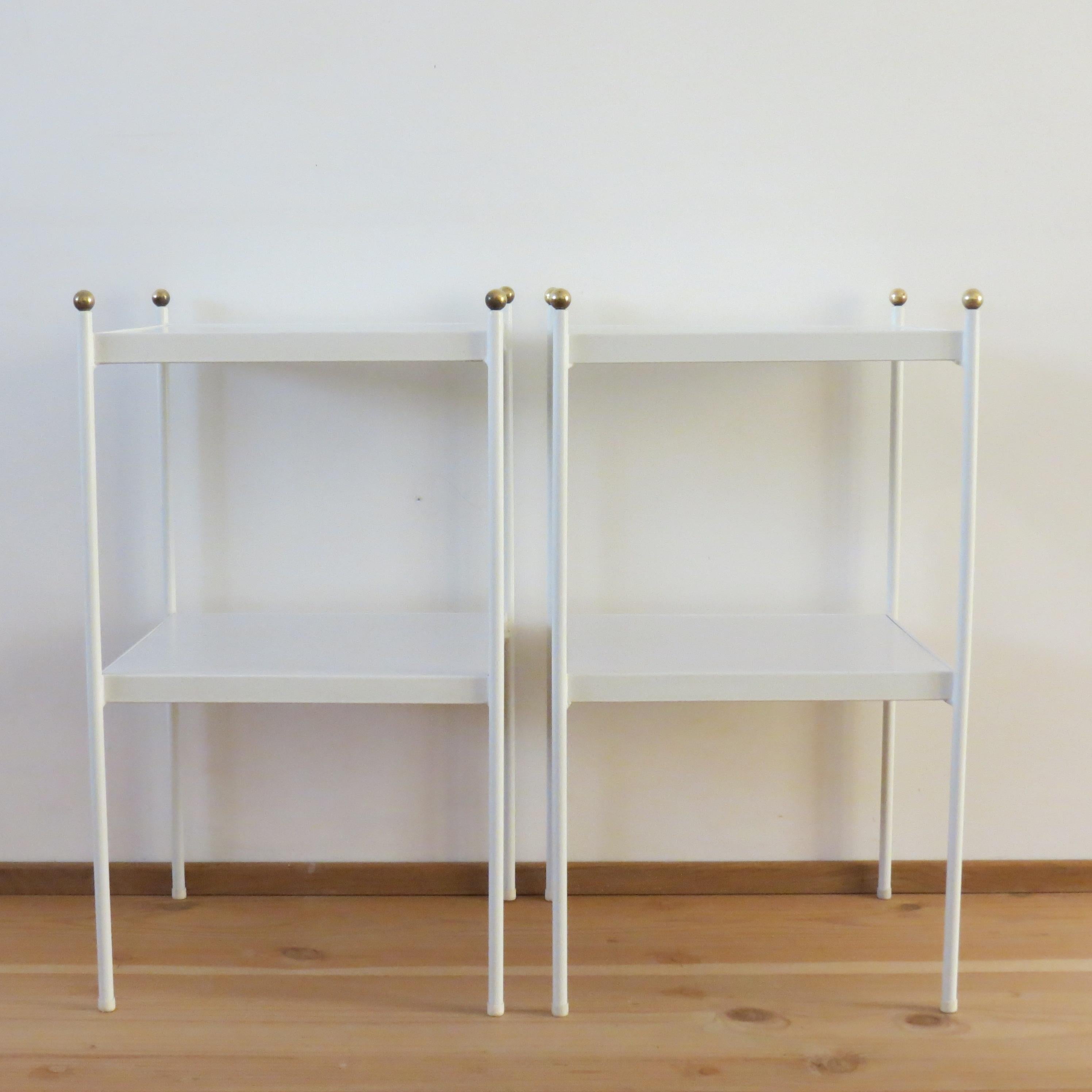 Pair of early 1960s metal bedside cabinets or side tables with very nice brass detail. Steel rod frames retain the original white enamel finish. White laminate shelves. Solid brass finial ball detail. Very good quality heavy tables.