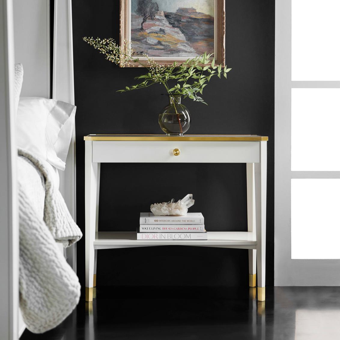 The refined design incorporates elegant brass trim along the top edge, matching brass leg caps, and a coordinating brass drawer pull that adds warmth and luxury to the minimalist form. The smooth lacquer finish highlights the table's precise