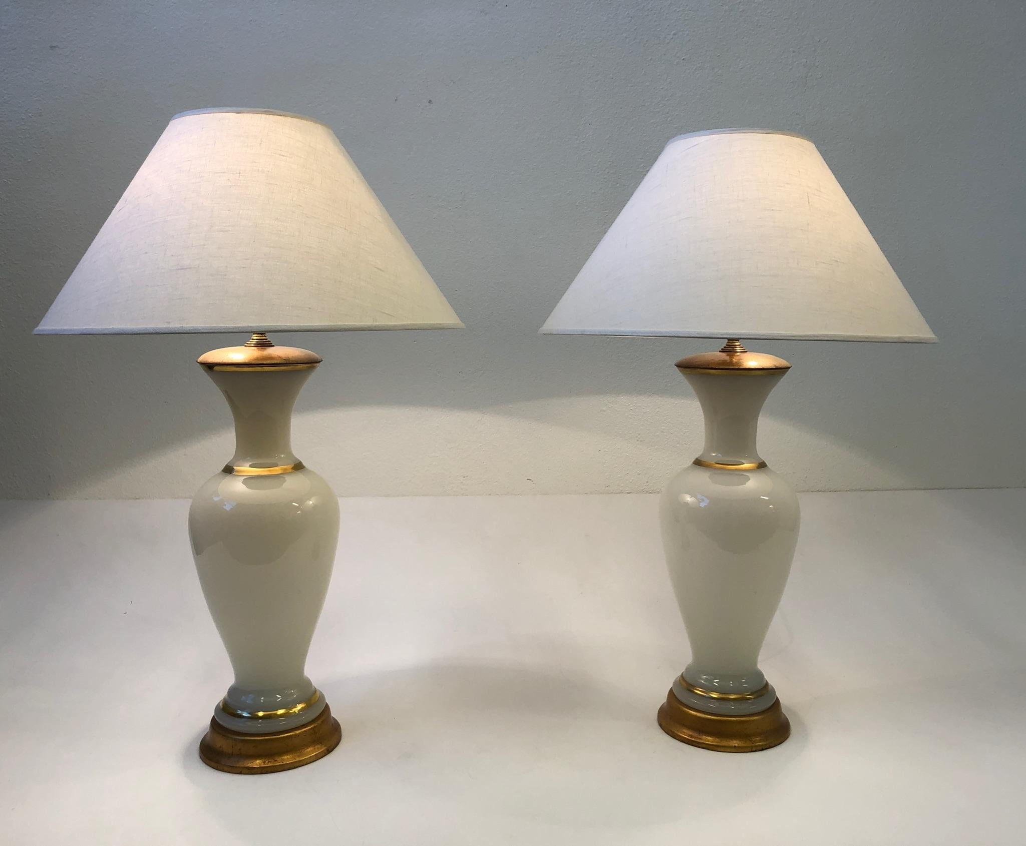 A glamorous pair of Italian white Murano glass and brass table lamps designed by Marbro Lamp Company in the 1960s. The lamps are constructed of Murano glass that’s hand painted with real gold stripes, brass hardware and the bases are gilded wood.