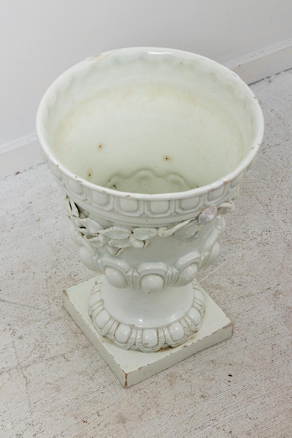 Pair of white pottery urns in the neoclassical style with Roman swags composed of foliage and fruit and rope gadrooning trim, circa 1950s. The piece is signed 