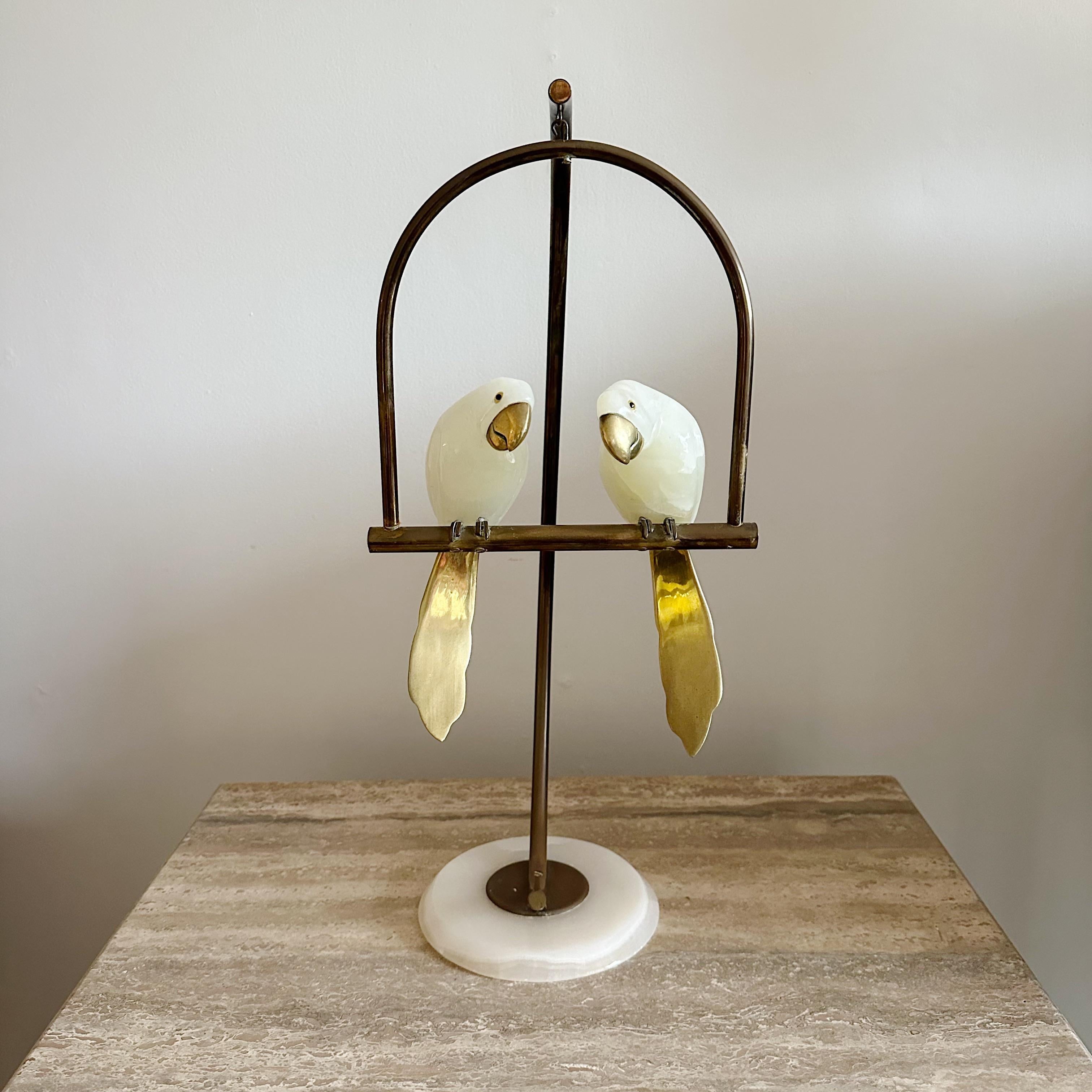 Sculpture of a pair of intricately carved white onyx bird from the 1960s on Brass stand. The sculpture depicts two birds with brass beaks and brass tails, perched on a brass swing, adding a playful touch to the classic design. The white onyx has
