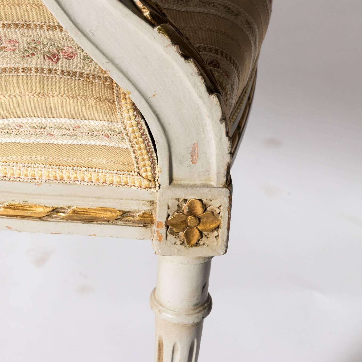 White painted Louis XVI style armchairs with rounded backs and gilded foliage detailing, circa early 20th century.
 