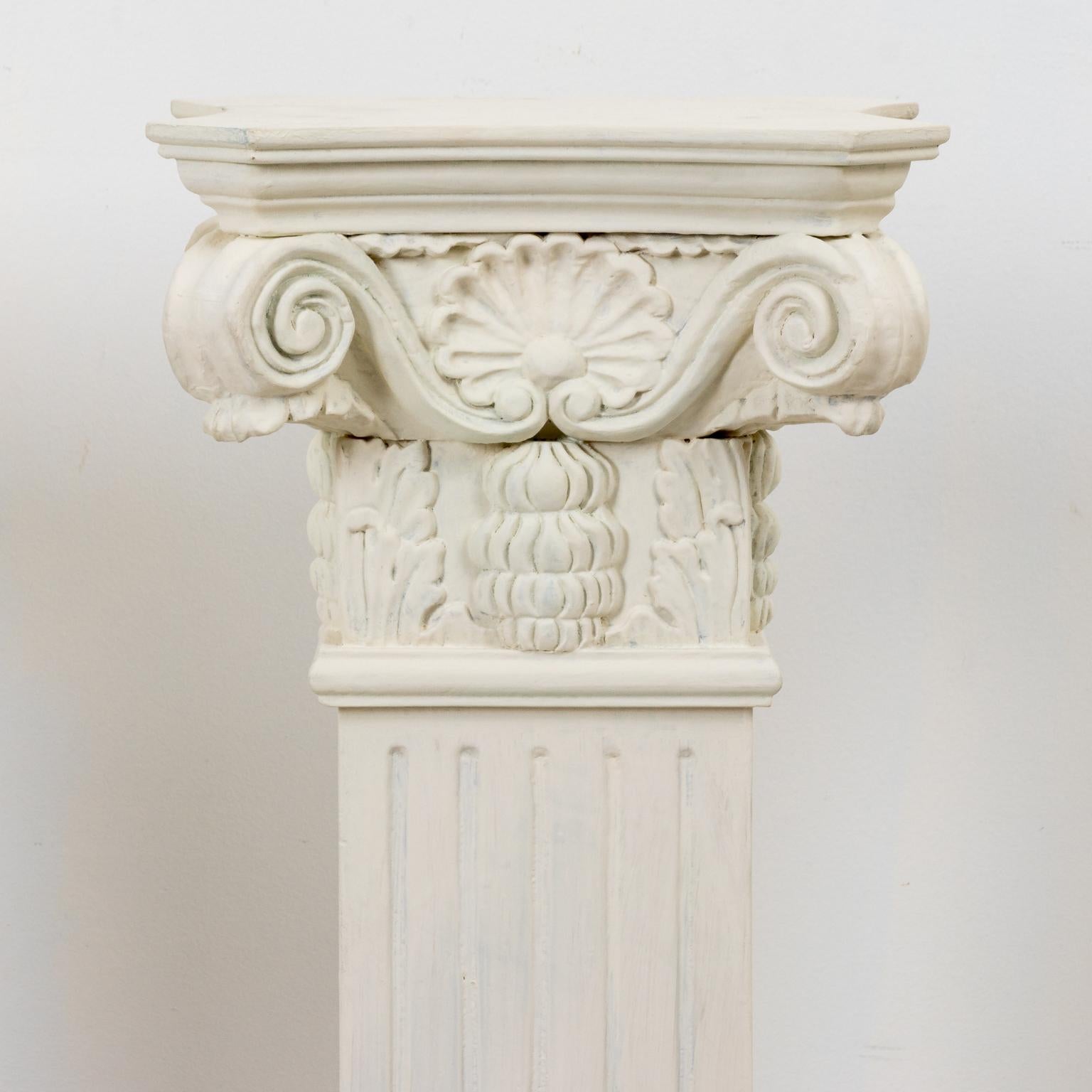 Pair of vintage white painted neoclassical style wooden carved pedestals with composite capitals, circa mid-20th century. The capitals are carved with scrollwork and floral detail along with a fluted column base. Please note of wear consistent with