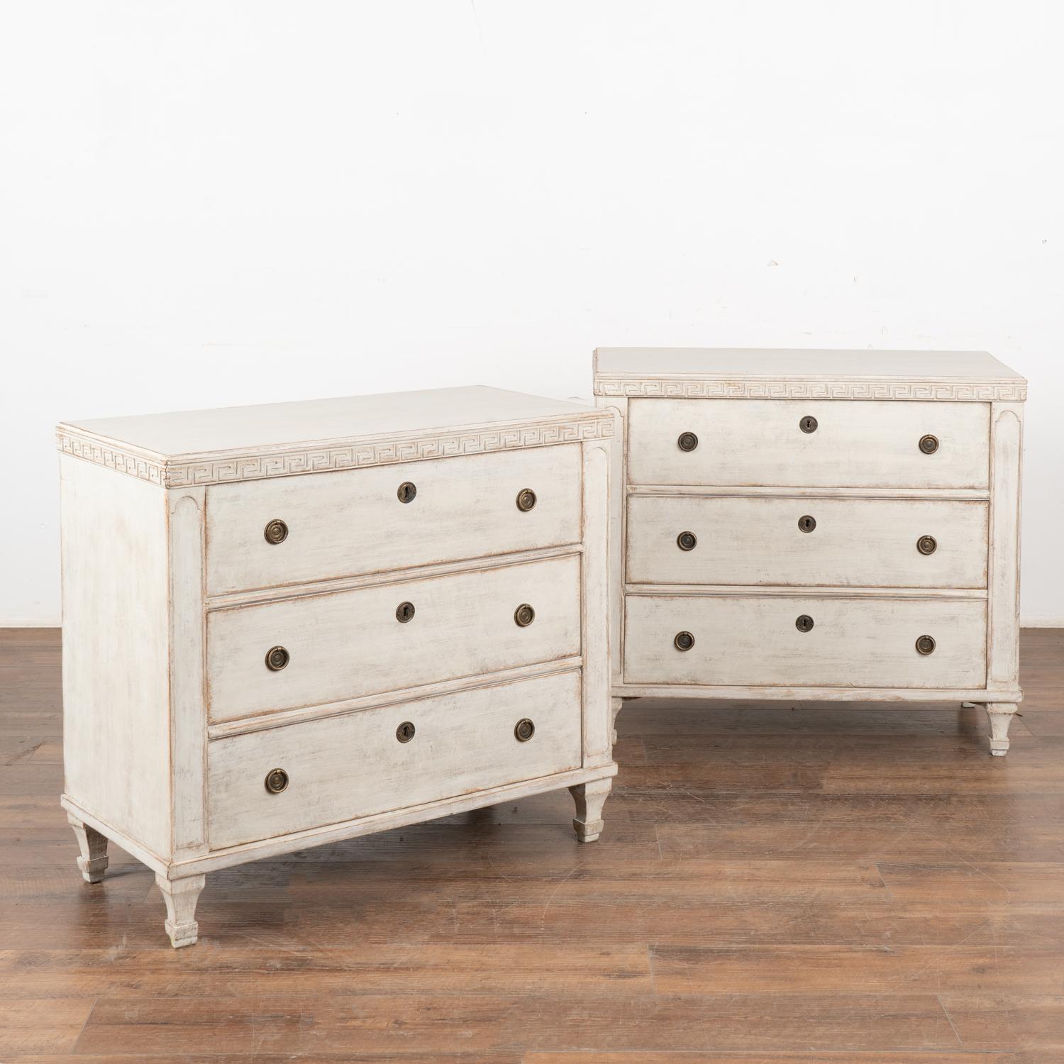 A pair of Gustavian pine chest of drawers with Greek key motif carved in upper molding resting on fluted feet.
The newer, professionally applied antique white custom painted finish is perfectly distressed to fit the age and grace of this lovely pair