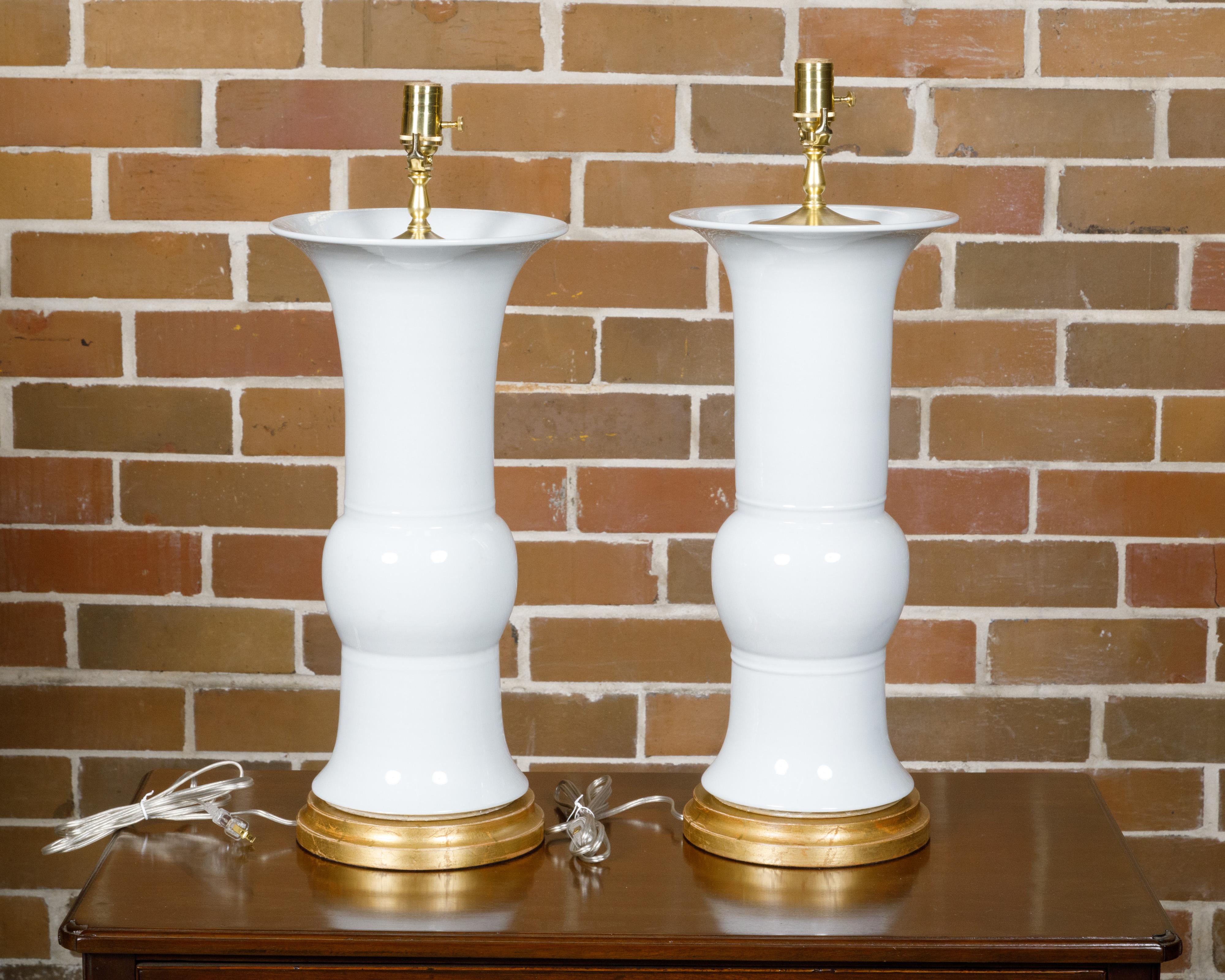 A pair of white porcelain table lamps on custom giltwood circular bases, professionally rewired for the USA. This elegant pair of white porcelain table lamps, set on custom giltwood circular bases, exudes a timeless charm and sophistication.
