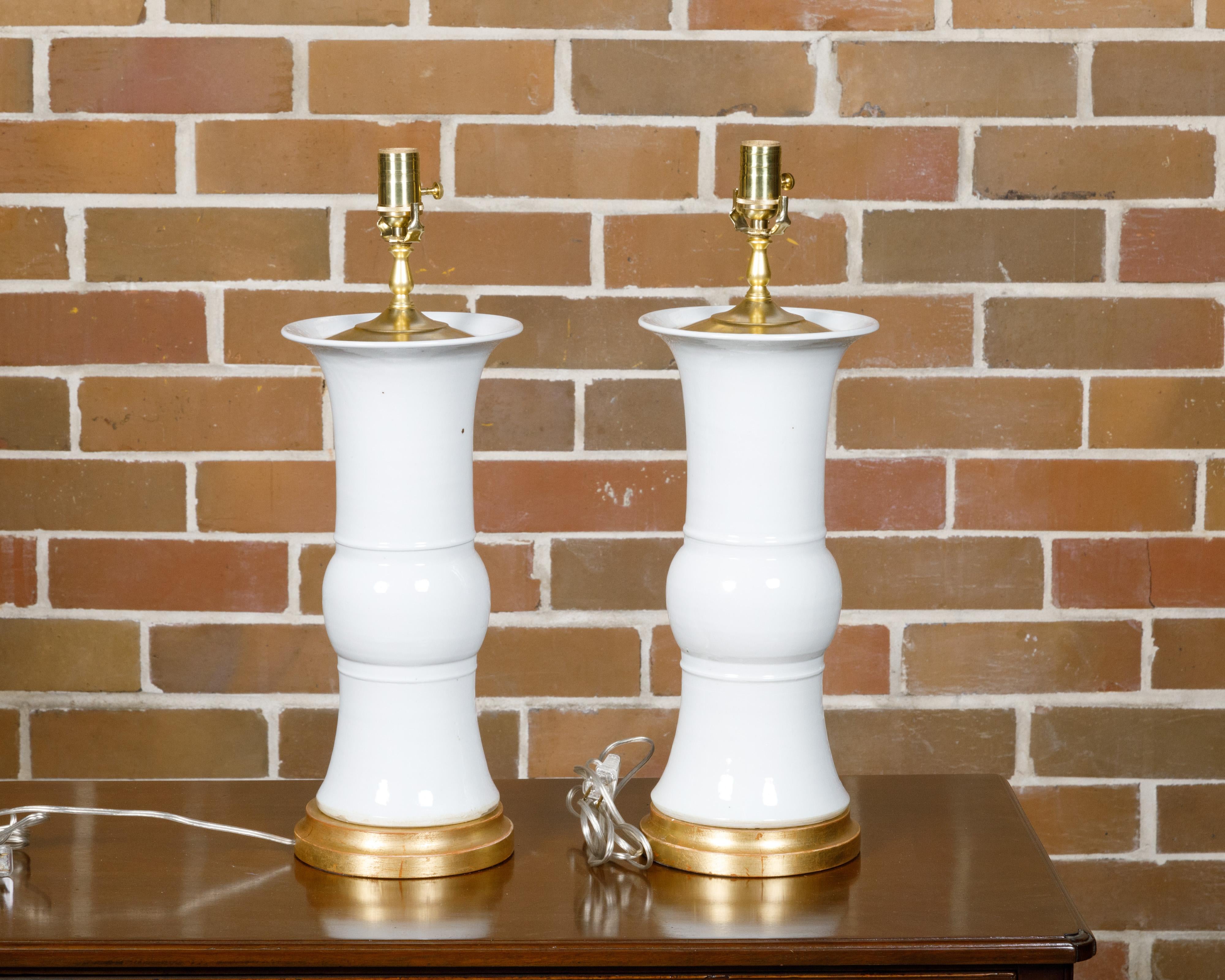 A pair of white porcelain table lamps on custom giltwood circular bases, professionally rewired for the USA. This elegant pair of white porcelain table lamps, set on custom giltwood circular bases, exudes a timeless charm and sophistication.