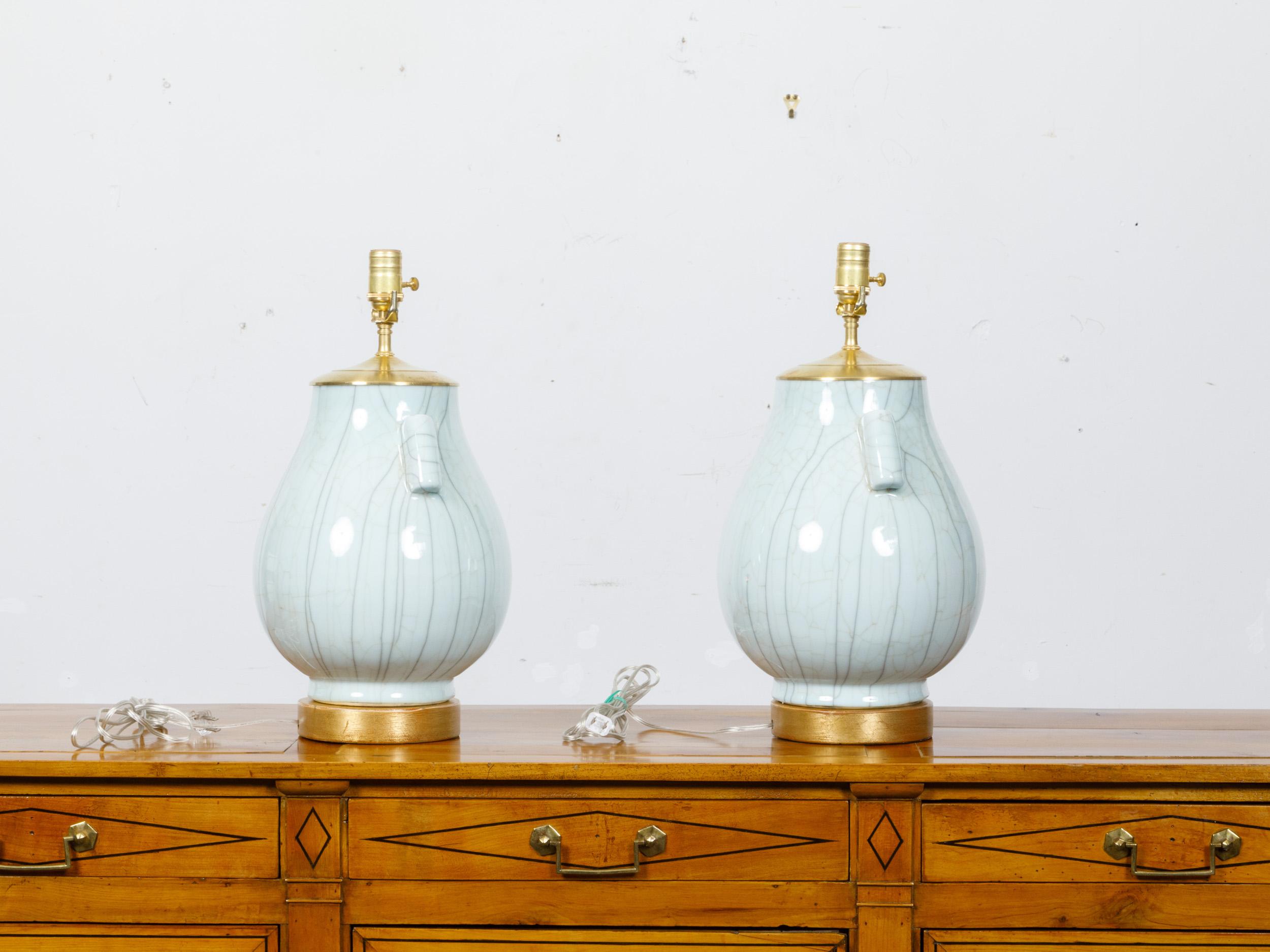 A pair of white porcelain vases with crackle finish and lateral motifs, made into single socket tables lamps wired for the USA and mounted on circular gilt wooden bases. This exquisite pair of table lamps features white porcelain vases with a