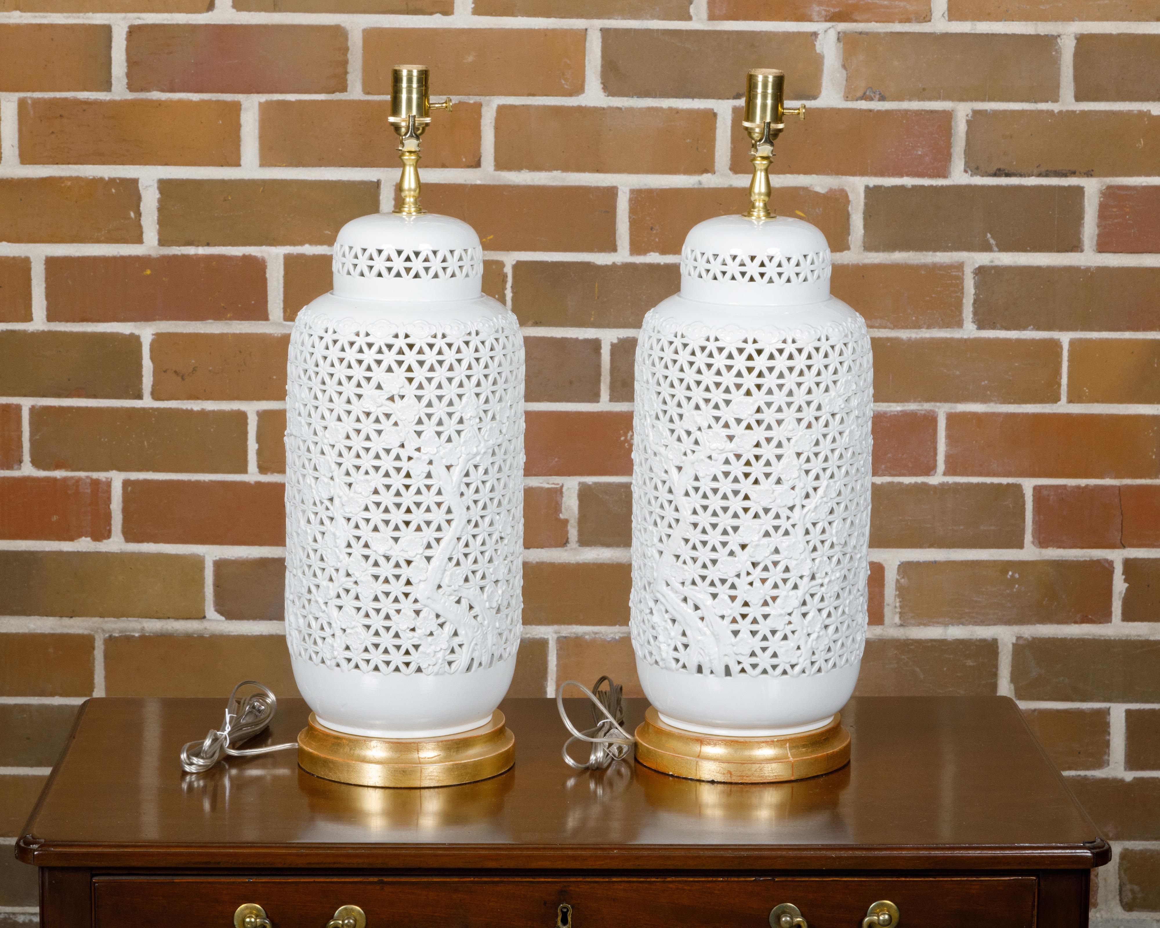 Paire de vases asiatiques en porcelaine blanche à décor floral et percé, datant d'environ 1900, transformés en lampes de table câblées pour les États-Unis et montés sur des bases circulaires en bois doré. Transformant avec élégance une paire de