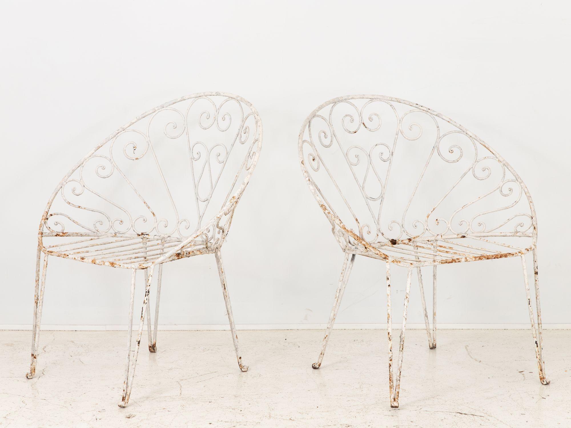 Introducing a sophisticated pair of 1970s French white painted iron garden chairs, elegantly designed to enhance the ambiance of any outdoor space. These exquisite chairs, skillfully crafted from iron, boast an unusual and whimsical design featuring