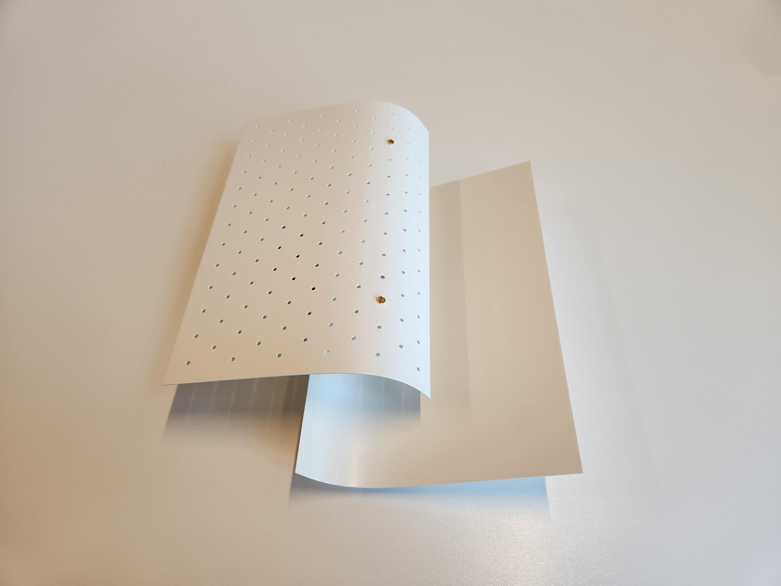 This lamp consists of 2 staggered layers of metal sheets. The light from the light bulb in between the 2 sheets is reflected against a solid steel sheet diffusing the light in the room while a perforated metal sheets in the front indirectly reflects