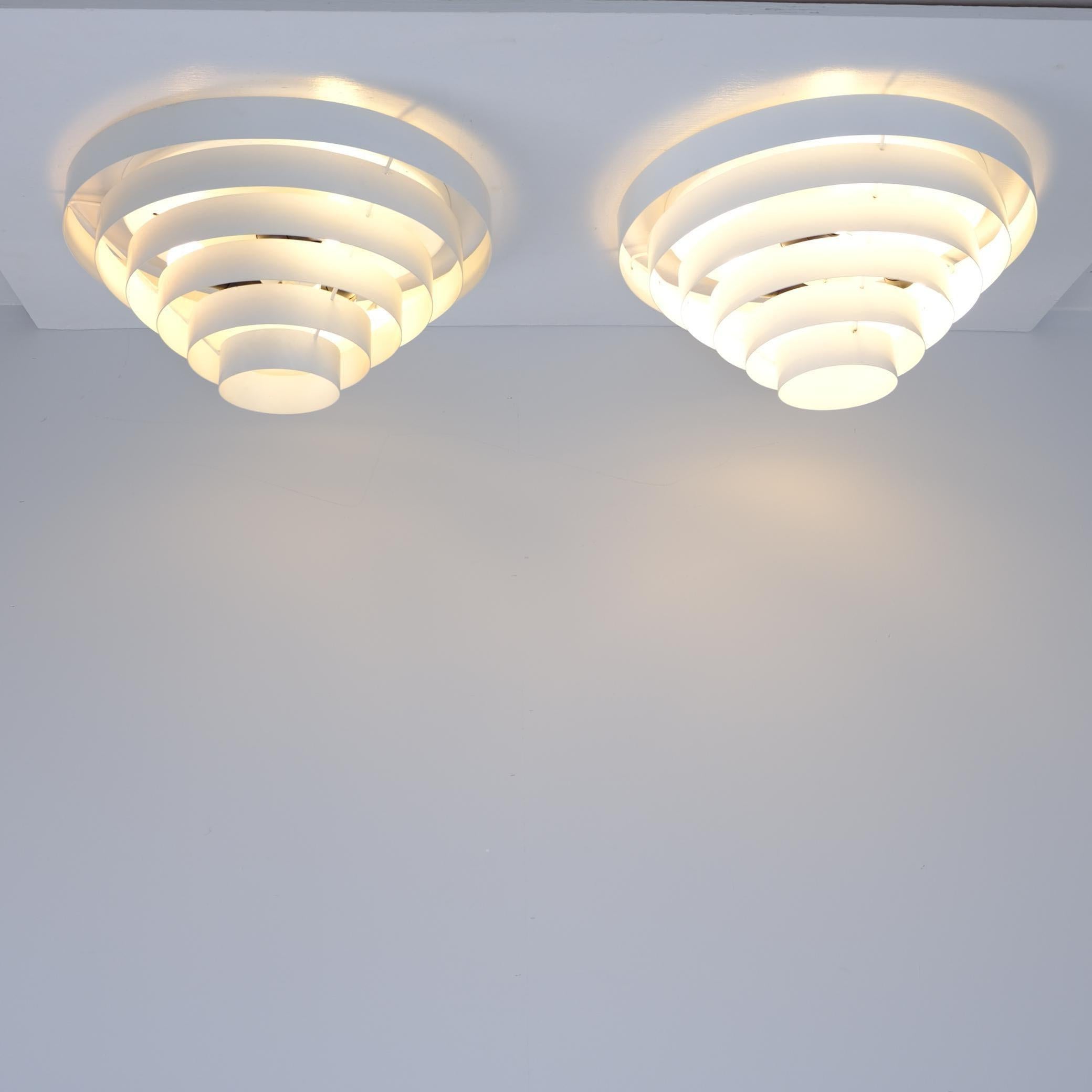 A pair of exceptionally refined modern ceiling lamps by the esteemed Finnish manufacturer, Itsu. Their design embraces elegant simplicity, featuring concentric metal circles that cast a soft, diffused glow from the  spaces between them. This