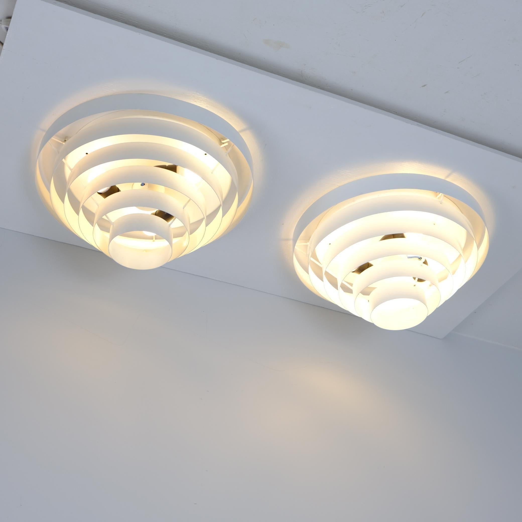 Un par de lámparas de techo modernas excepcionalmente refinadas del estimado fabricante finlandés Itsu. Su diseño adopta una elegante sencillez, con círculos metálicos concéntricos que proyectan un suave resplandor difuso desde el  espacios entre