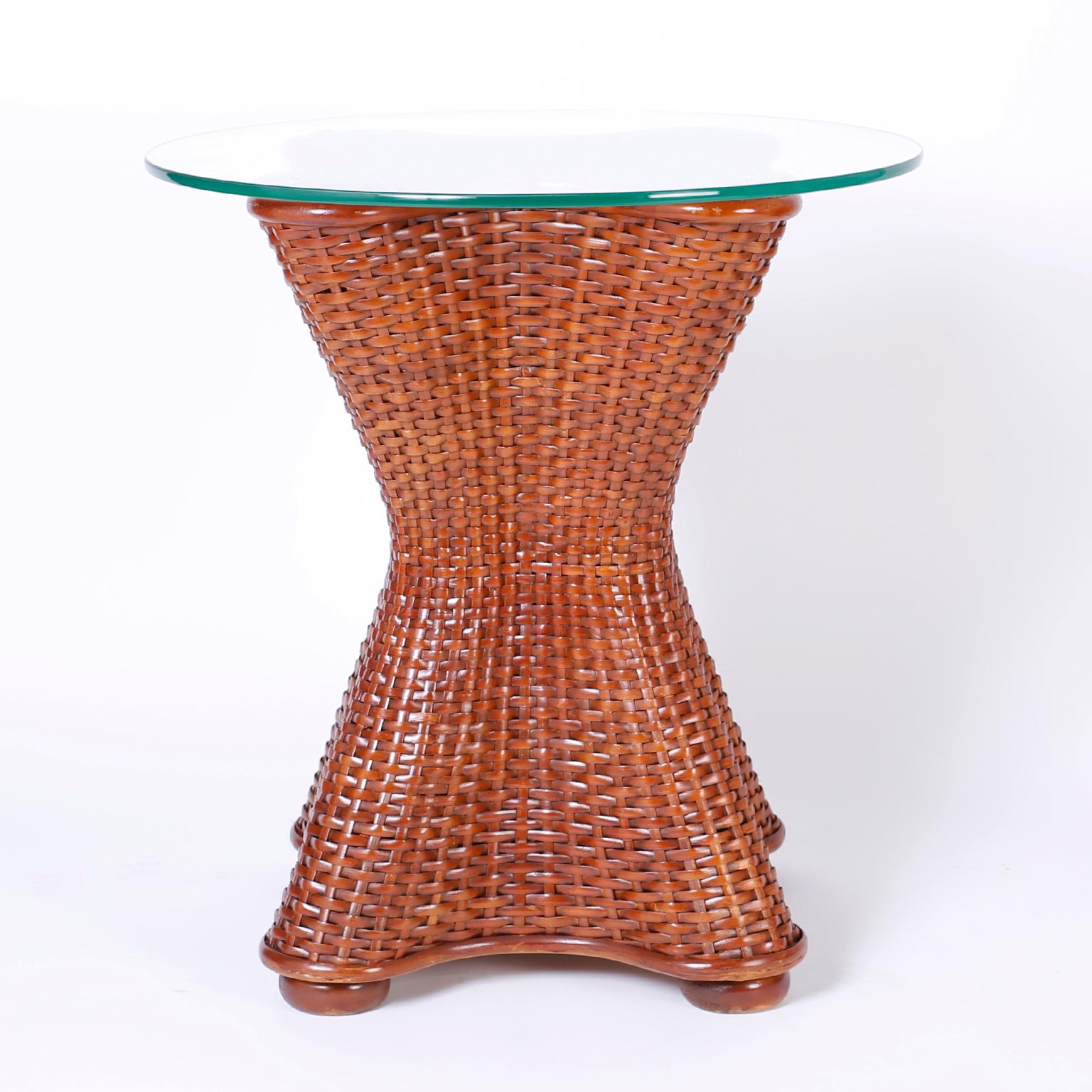 Midcentury wicker and rattan stands with round glass tops and a classic hour glass form on bun feet. Can also be used as a dining table base.