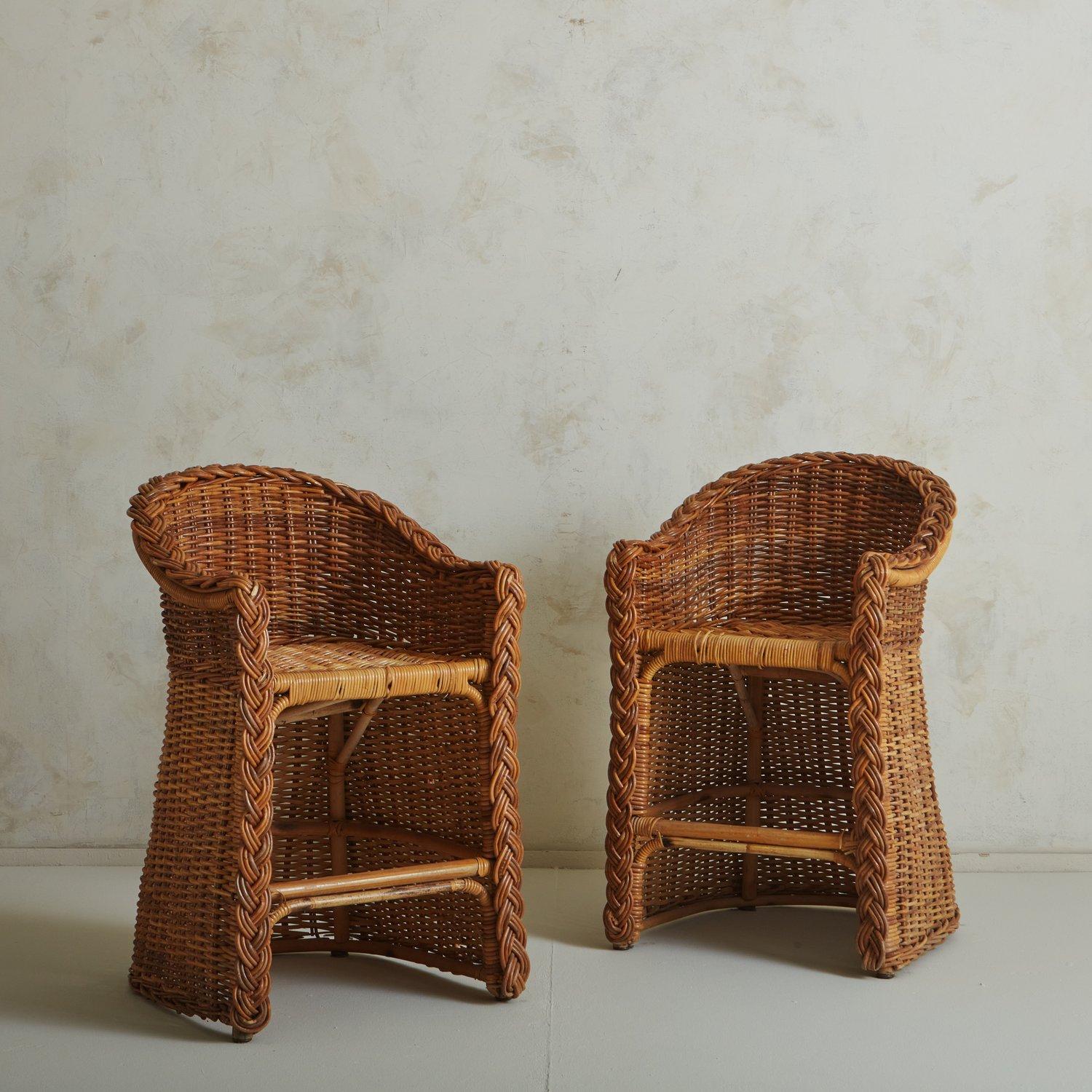 A pair of vintage wicker and cane bar stools with barrel frames and a beautiful braided trim. These stools have curved armrests and a foot support bar. We love the subtle color variations, warmth and durability of these natural materials. 20th