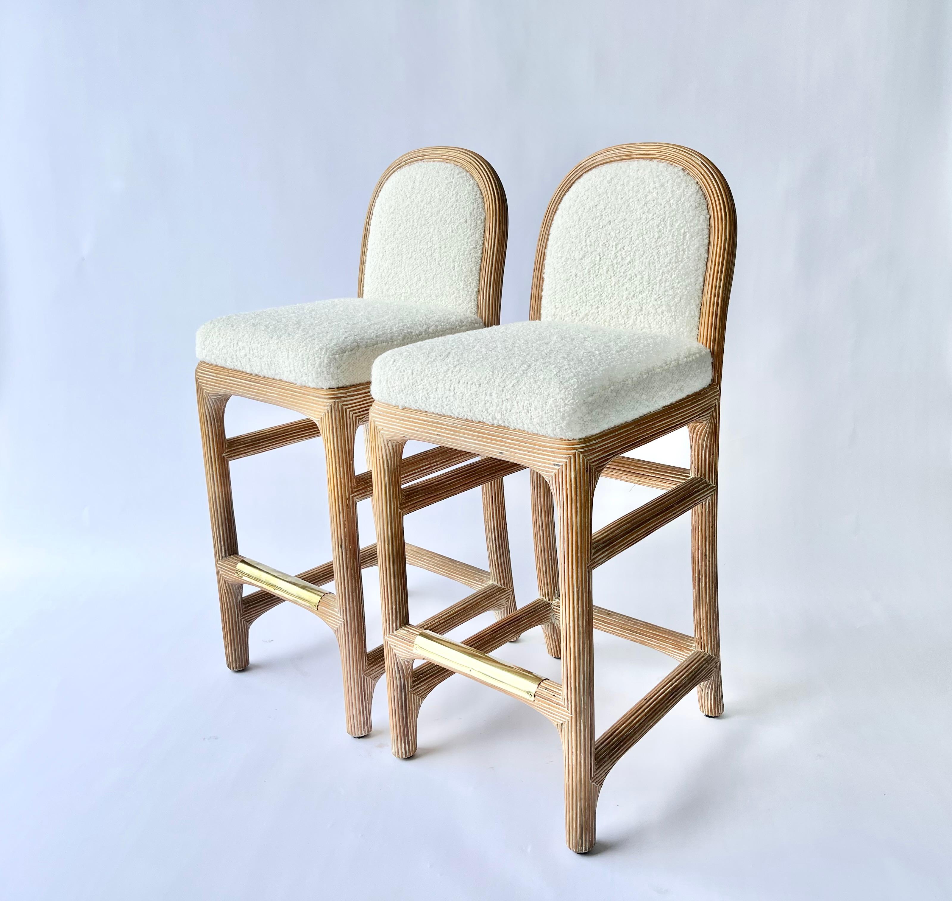 Pair of Wicker Pencil Reed Upholstered Bar Stools after Gabriella Crespi, 
with brass foot rail protectors. Freshly upholstered in Kravet Ivory Nubby Boucle.
Ready for a new home.