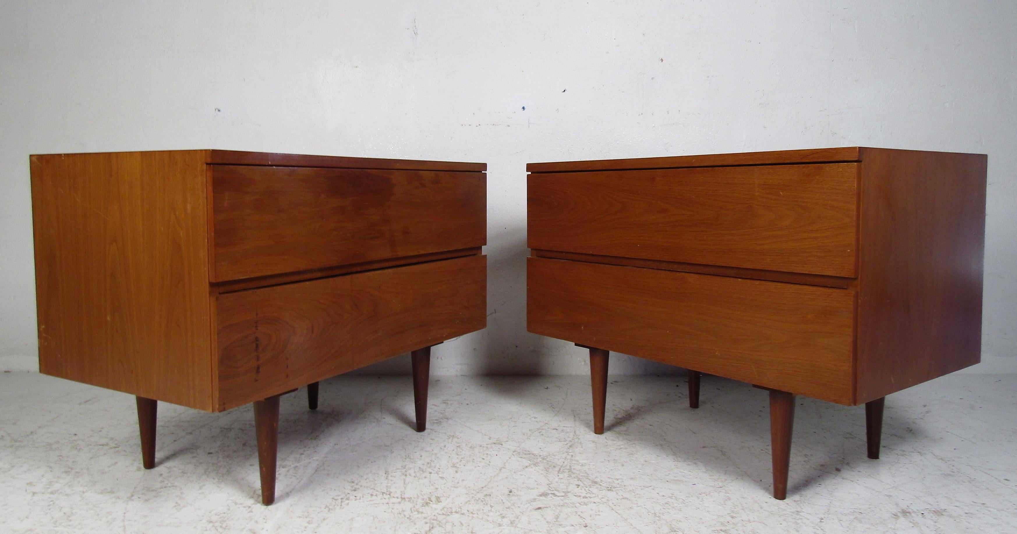 A beautiful pair of vintage modern two-drawer nightstands with a finished back. This well-made pair offer ample storage space within there two large drawers. An unusual wide design with hidden drawer pulls and stubby tapered legs. These make the