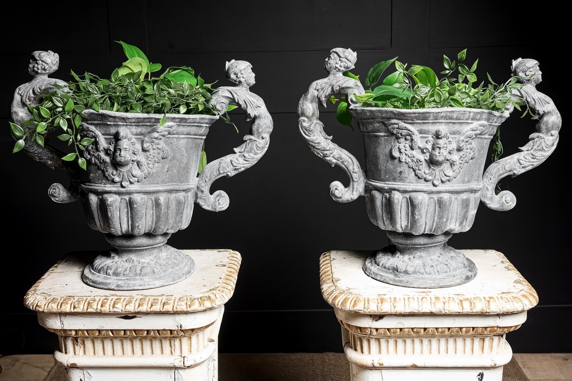 Coppia di urne di piombo modello William & Mary. Realizzato nel XIX secolo dalla Bulbeck Foundry. Con due maniglie a forma di cariatidi e foglie d'acanto, che incorniciano un'urna con decorazioni, decorata con un cherubino, su una base circolare.