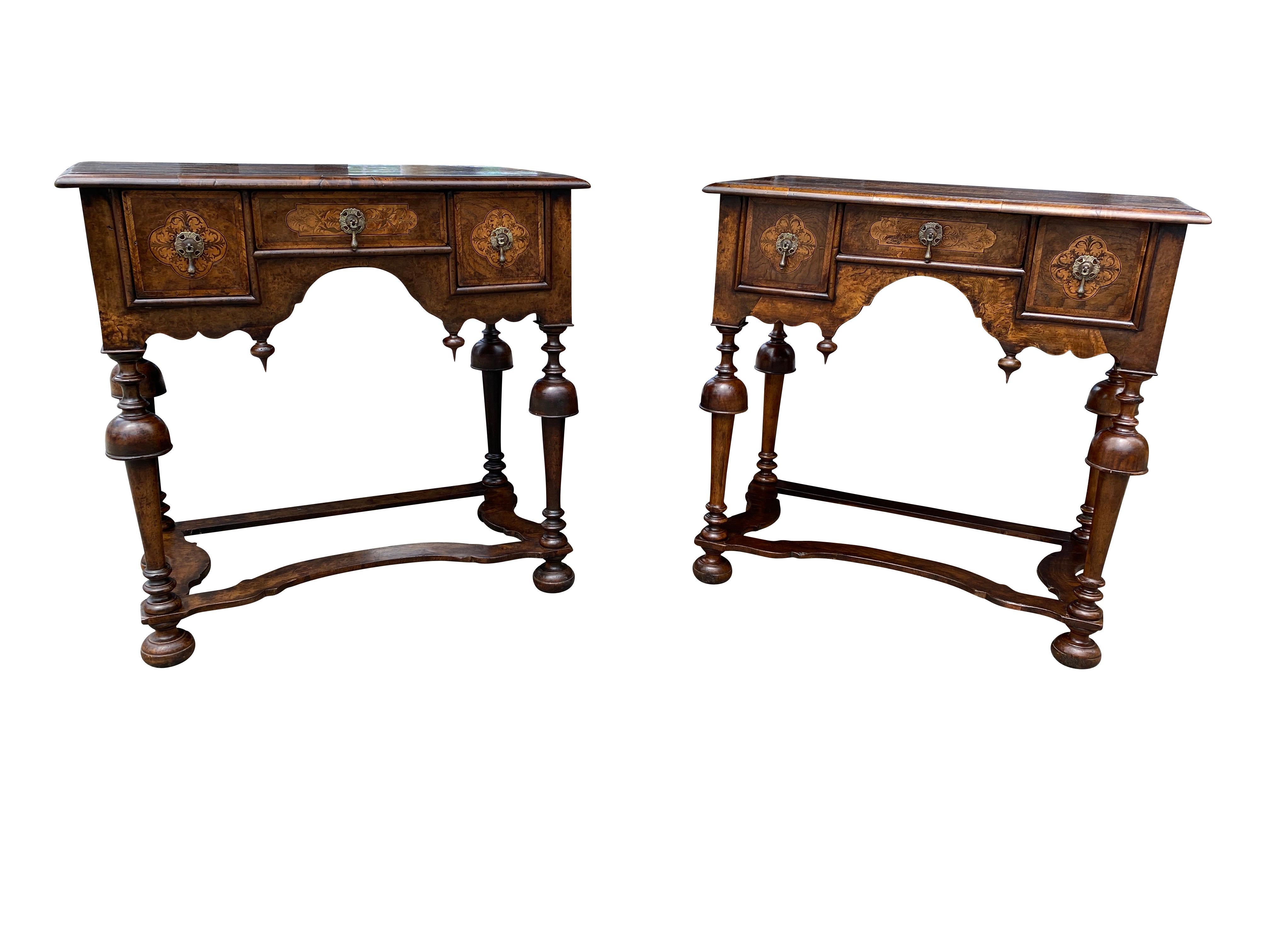 Each with rectangular tops with central lozenge seaweed marquetry panels and cross banded edge over a central drawer franked by a pair of drawers, raised on trumpet form legs joined by flat stretchers and bun feet.