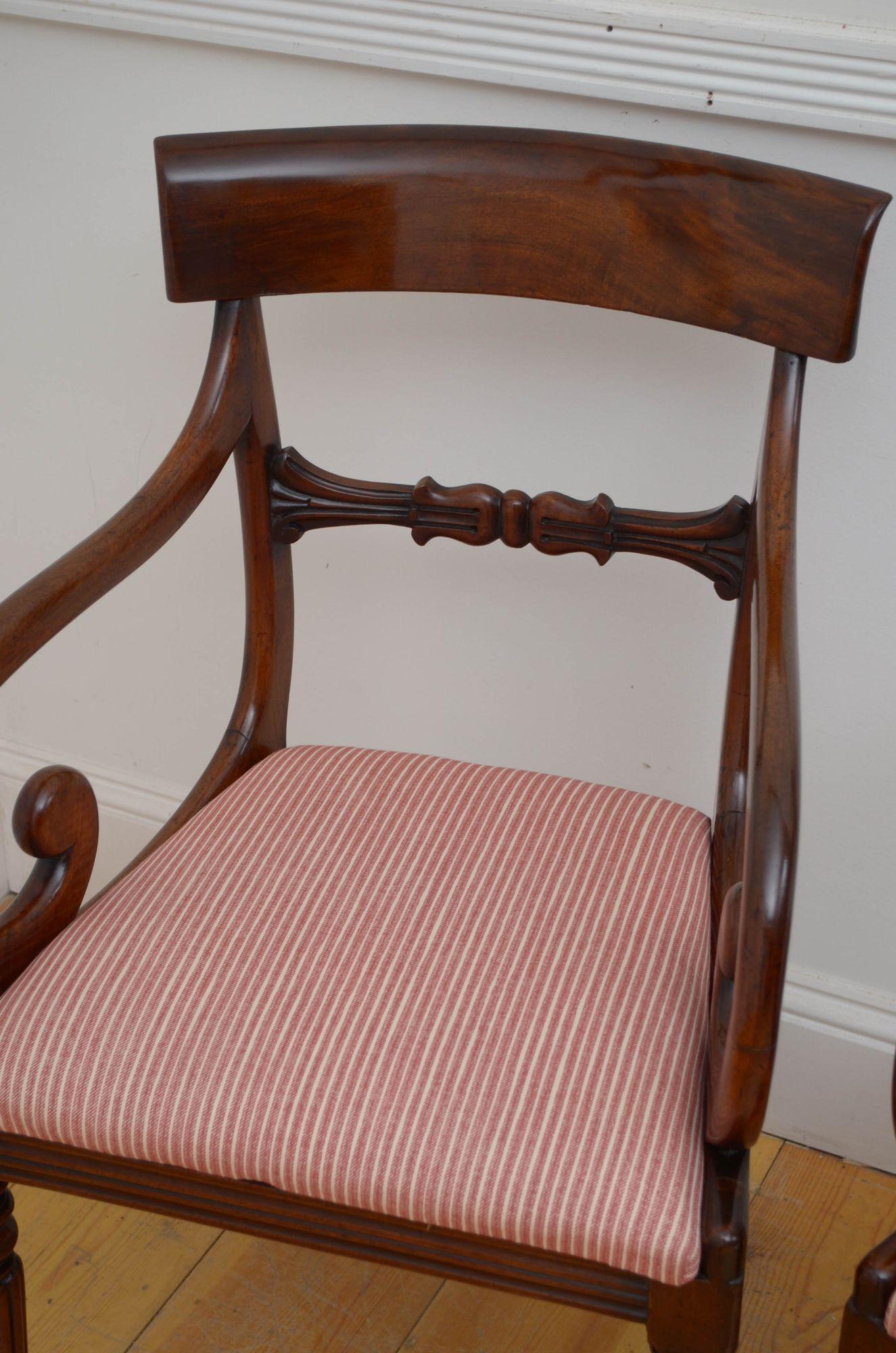 J020 Pair of antique carver chair in mahogany, each having shaped top rail above carved mid rail and drop in seat flanked by open scroll arms, all standing on turned and fluted legs. This antique pair of chairs is in home ready condition.
