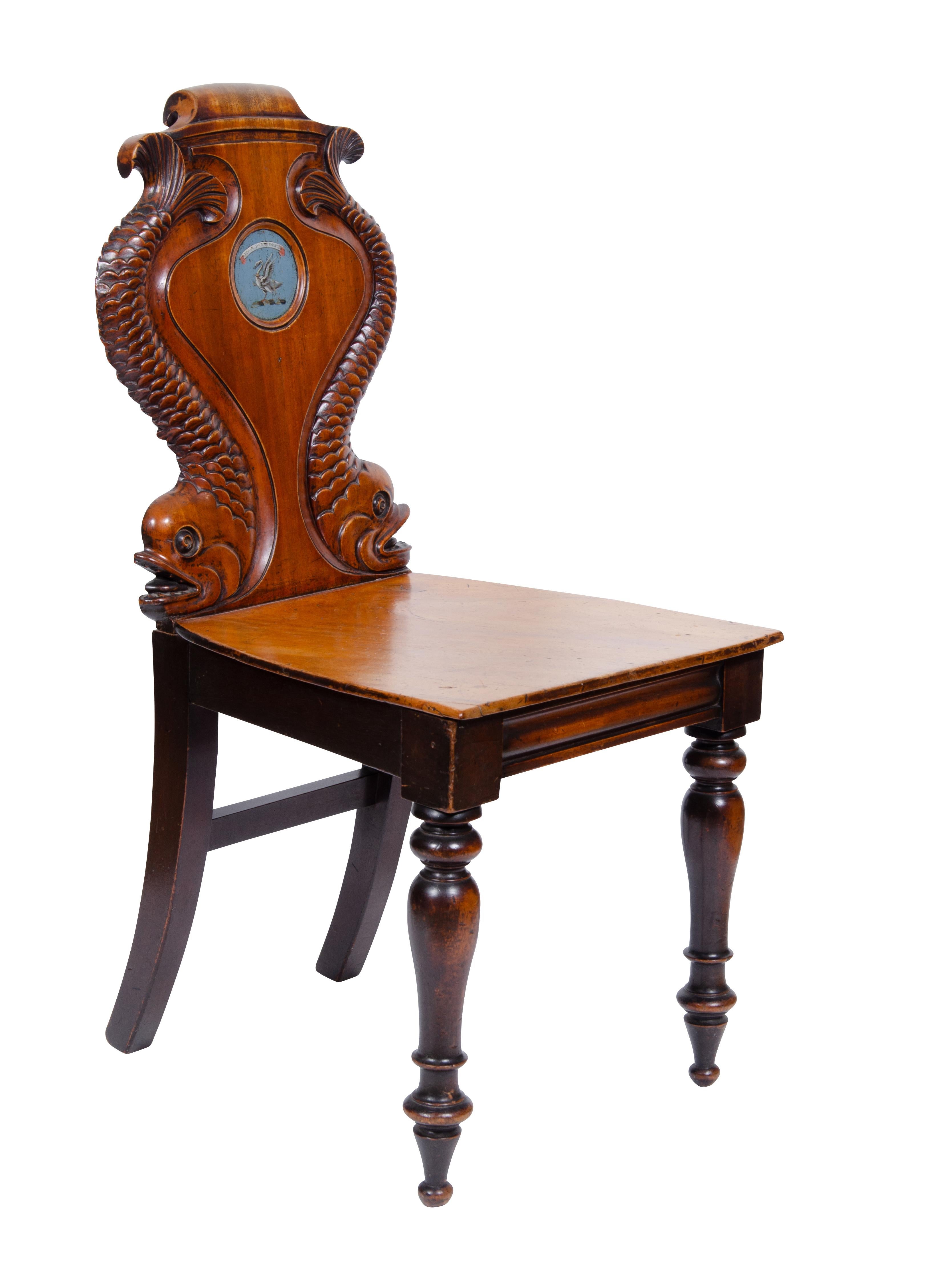 Unusual, each chair back with two carved dolphins and central painted coats of arms, solid wood seats raised on circular tapered legs. These chairs are part of a larger set which would have been placed in a hallway in an upscale British home.