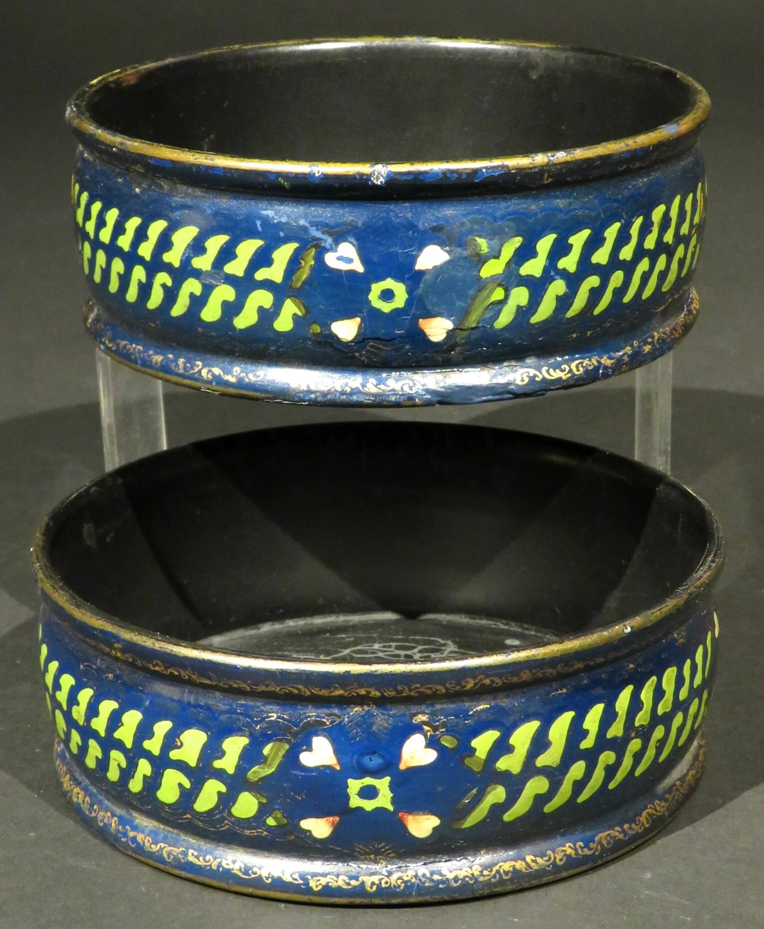 Both coasters decorated with hand painted repeating bands of green geometric motifs interspersed by a quadrant of heart-shaped petals set against a dark royal blue field, the base and rim showing remnants of gilding. Both remain in sound condition