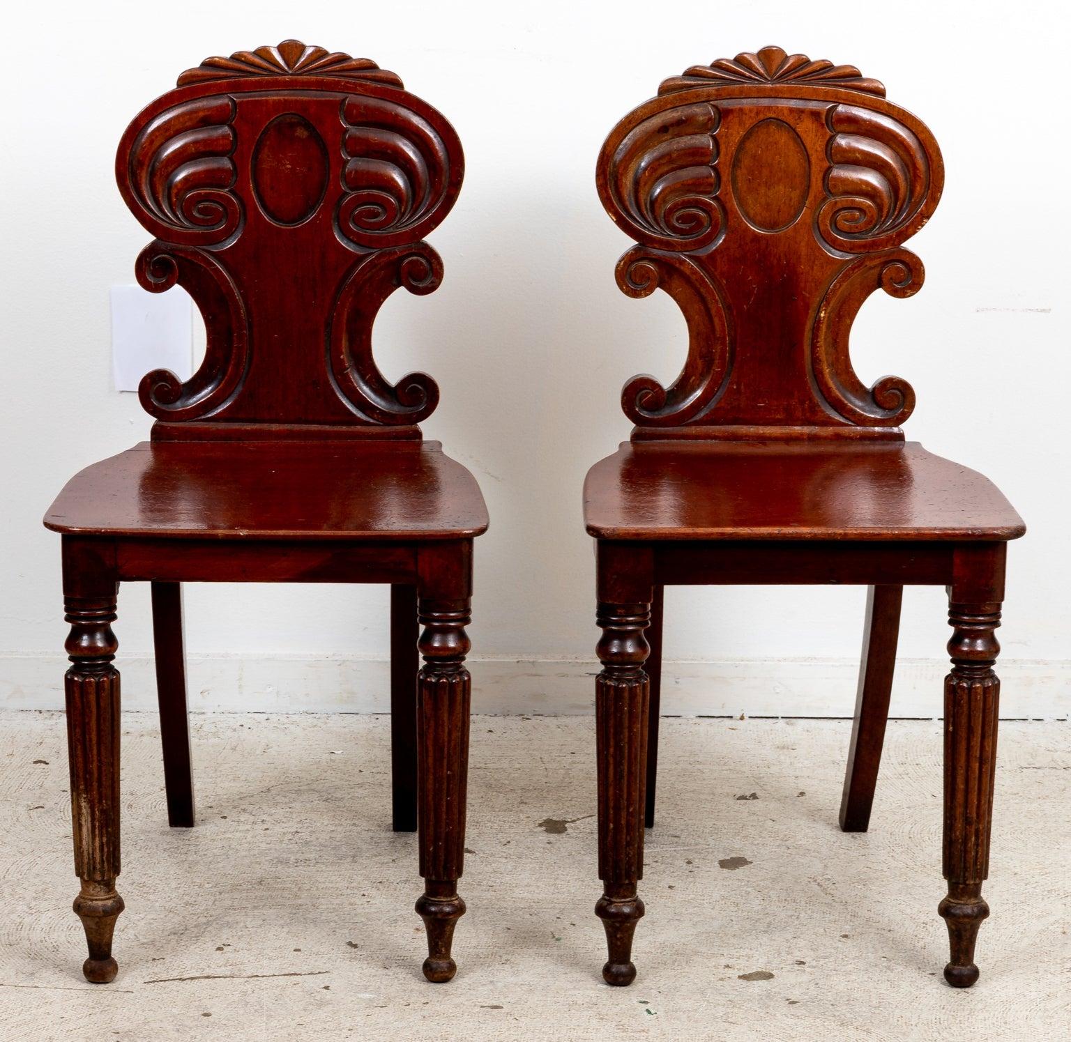 Pair of English William IV style Walnut hall chairs carved with fluted, turned legs and c-scroll motifs on the seat back. The seat back is also decorated with a central oval shaped medallion and a fan design on the top rail. Origin unknown. Please