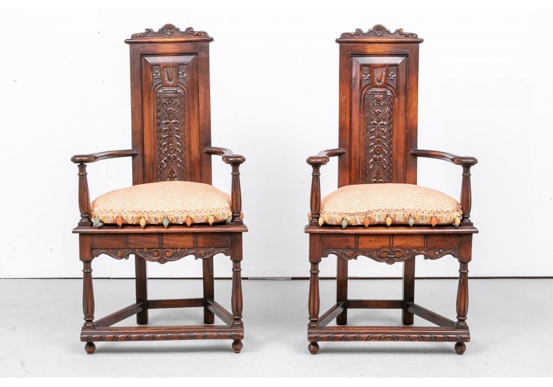 Pair of walnut hall chairs with flared and welcoming arms, a slight triangular form with a heavily carved raised panel backrest, scalloped crest with floral and scrolling foliate motifs. The chairs with a tapering stretcher having a carved spiral