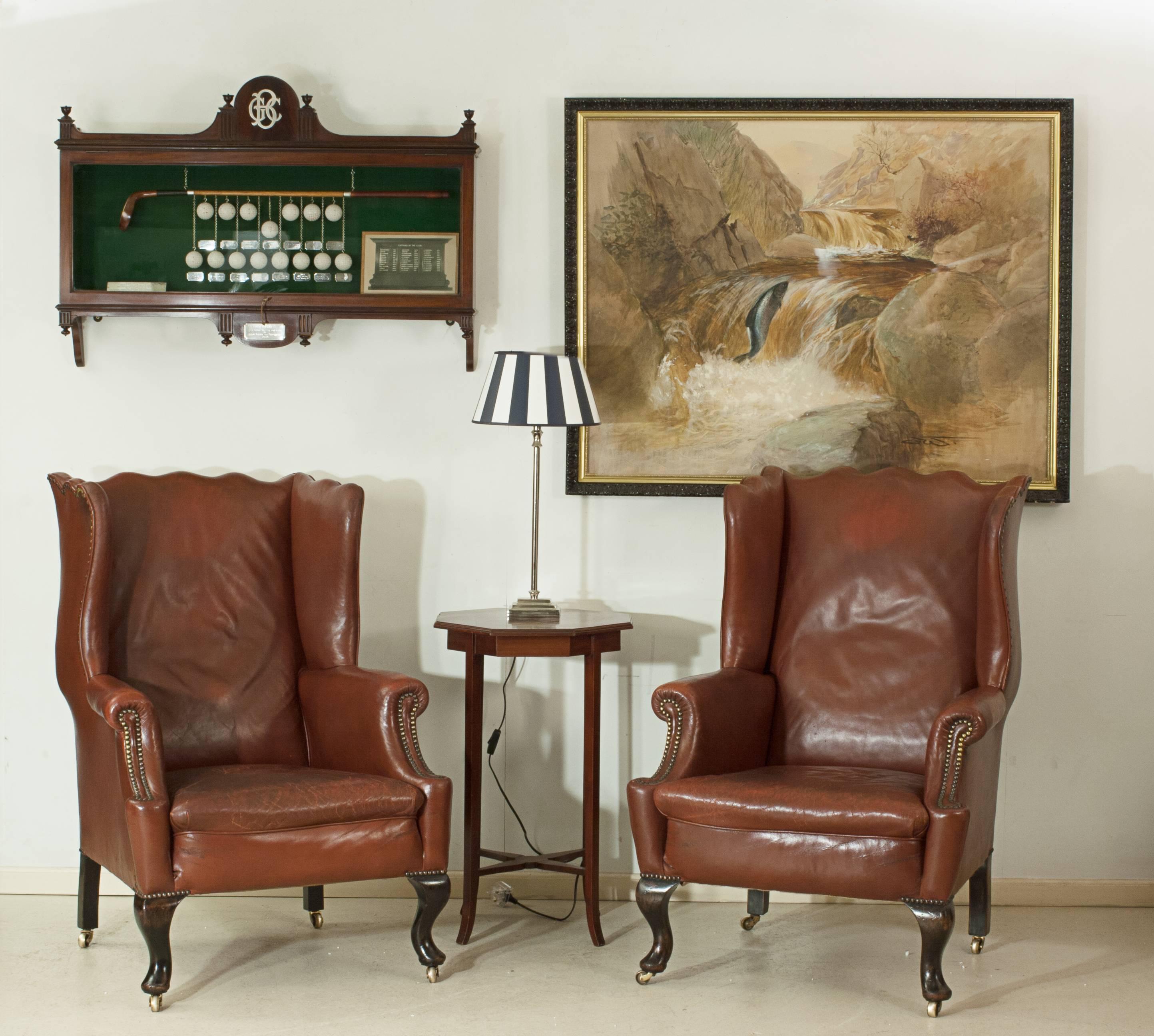 Red leather wing armchairs.
A pair of early 20th century red leather wingback chairs. The lady's and a gentleman's wing arm chairs are of slightly differing sizes, well-proportioned high backs with oversized wings, scrolling arms and with brass