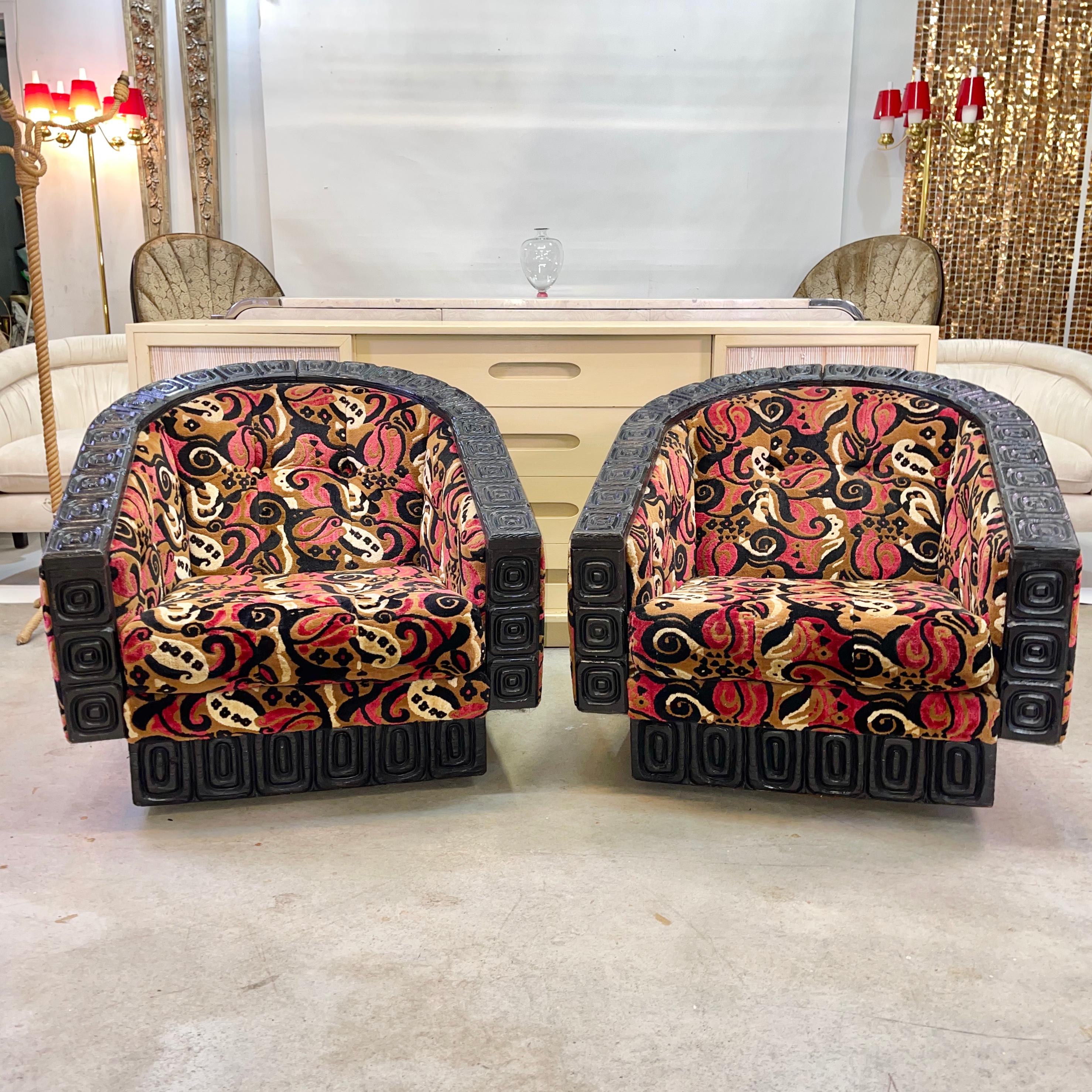 Tiki chic pair of barrel back swivel lounge chairs designed by William Westenhaver with tropical inspired carved cedar and textured velvet upholstery.
Chairs have a recessed carved wood square plinth under which is an unseen round swivel platform