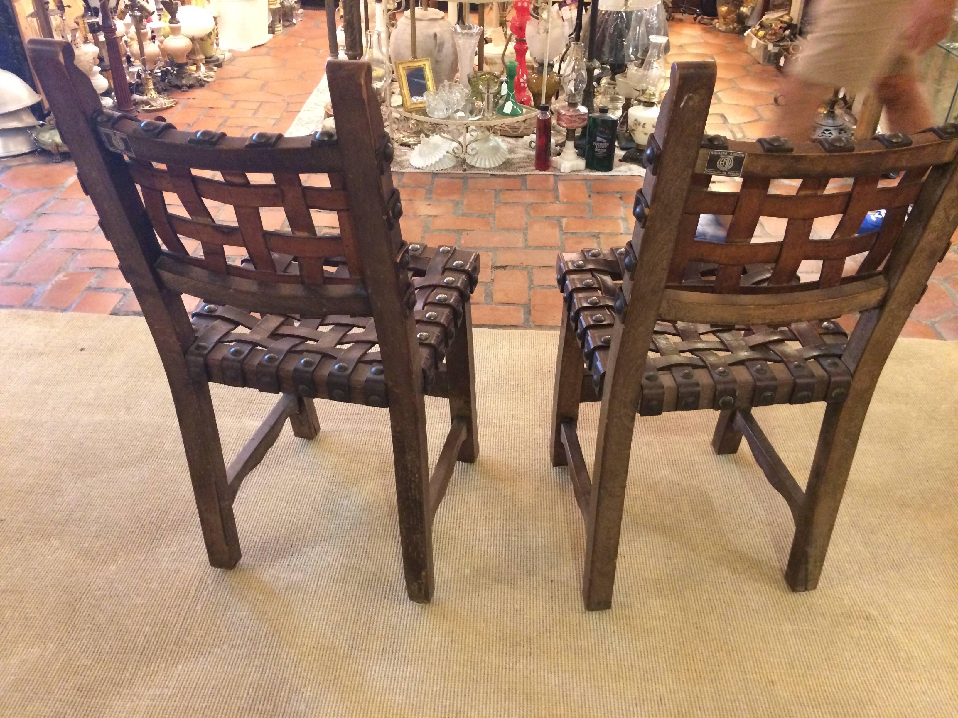 Two antique Spanish side chairs having wonderfully carved wood bases and rich heavy woven strap leather seats and backs with big masculine nailhead studs. By Navarro Argudo, Spain. Leather has natural aged distressed patina.