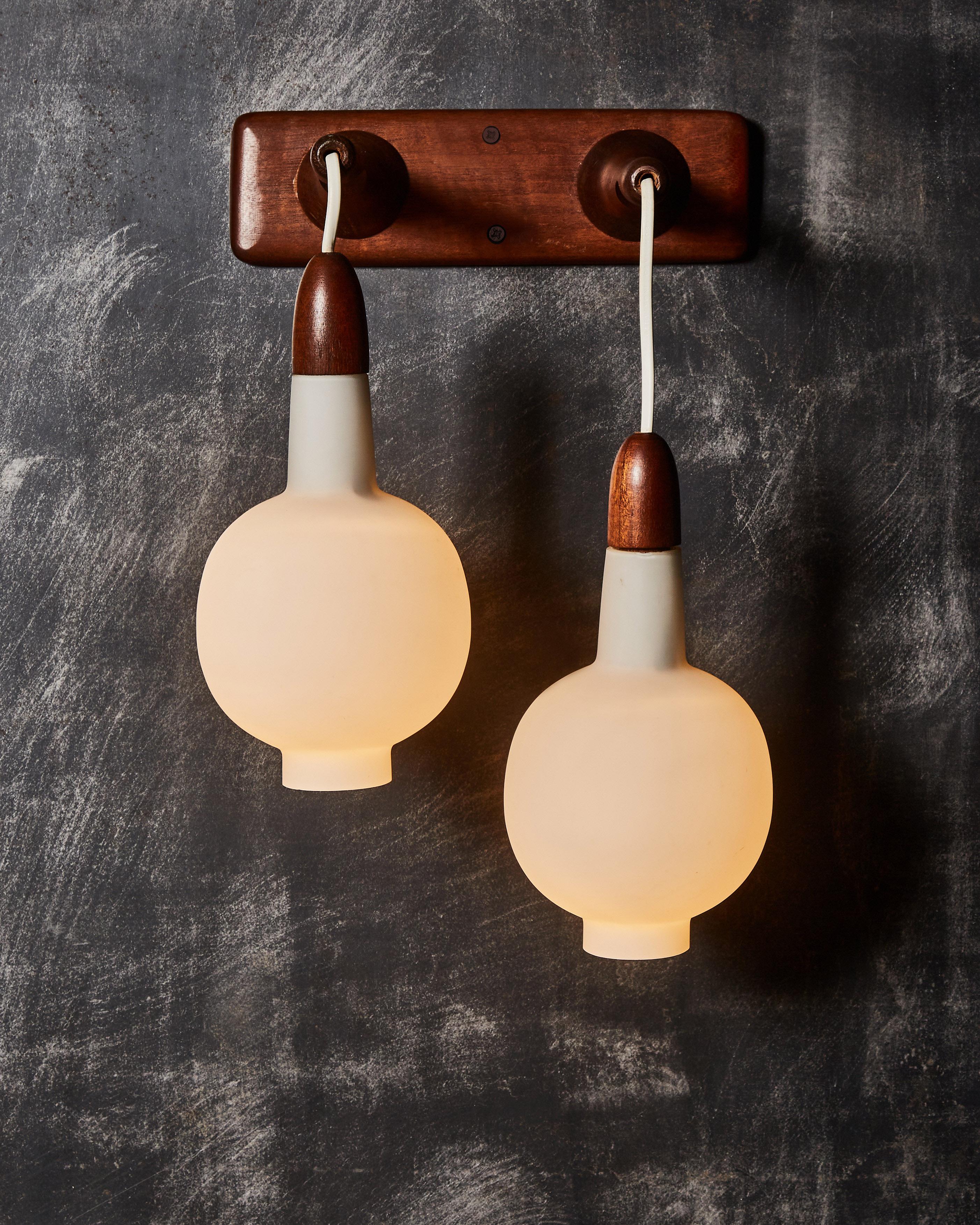 Pair of mid-century wall sconces made of a dark wood backplate and arms and two opaline glass lanterns.