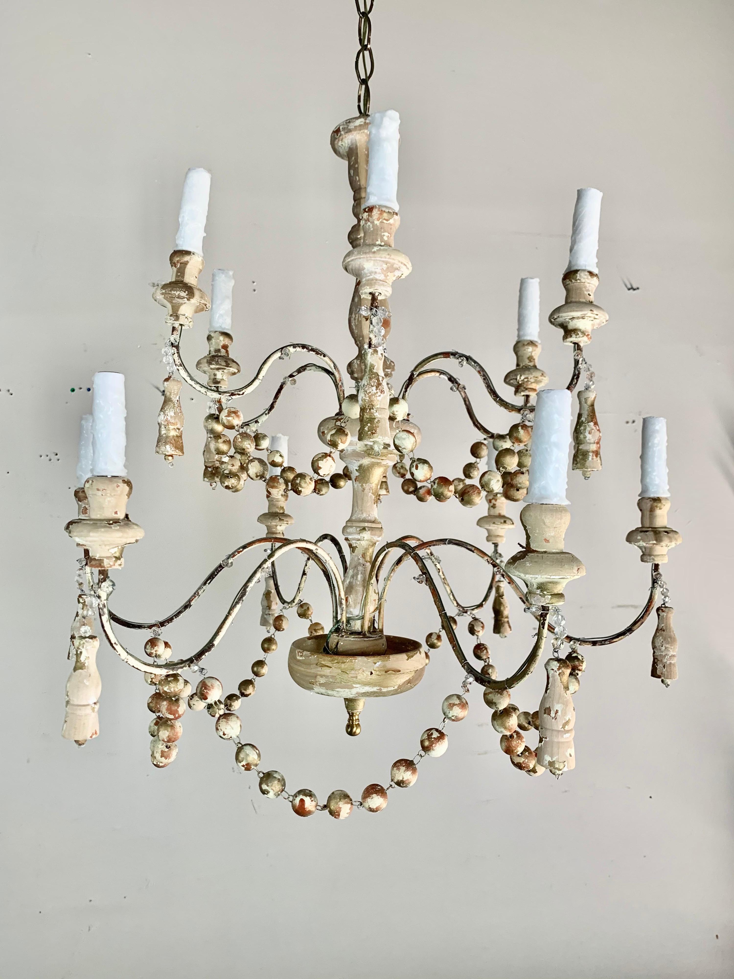 Pair of Italian painted wood beaded chandelier with garlands hanging throughout the 12 arms of the chandelier. There are hand carved tassels hanging throughout as well. The paint of the chandelier is beautifully distressed with some natural wood