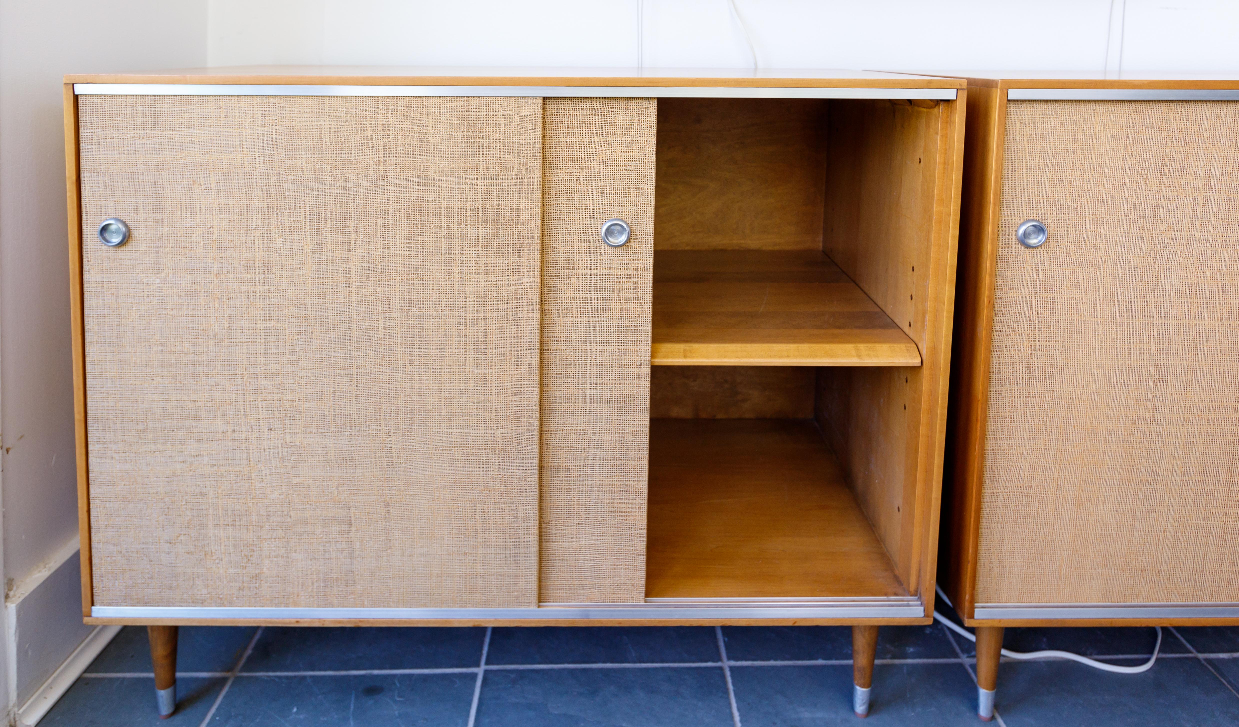 Pair of wood cabinets with sliding grass covered doors and interior shelves with mat metal details
By Herman Miller.